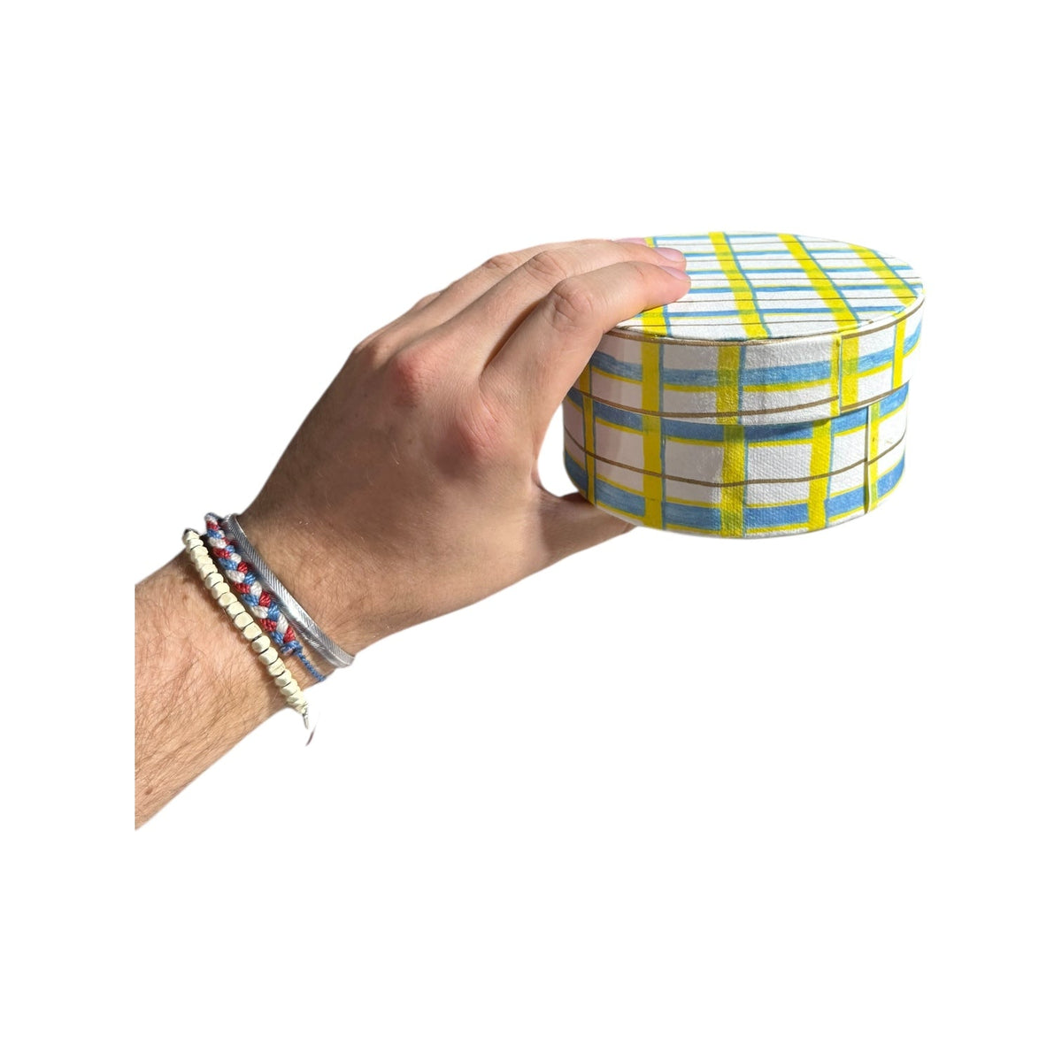 Hand holding a round handmade recycled paper gift box with green and yellow plaid stripes.