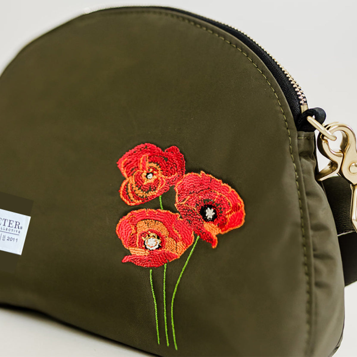 Olive nylon pouch close-up with red flower embroidery and stitched zipper edge