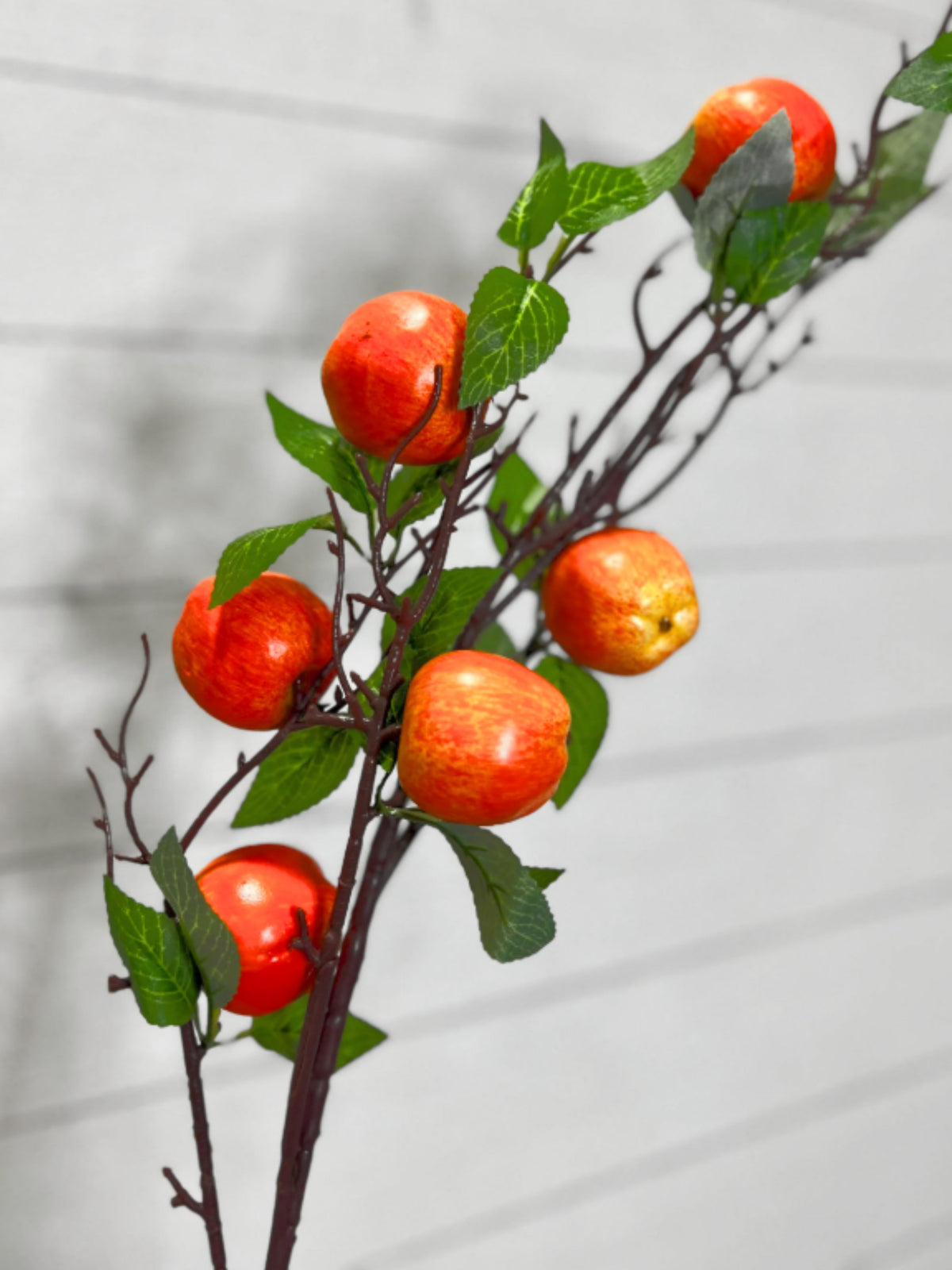Artificial apple stem with red and orange apples and green leaves on curved branch