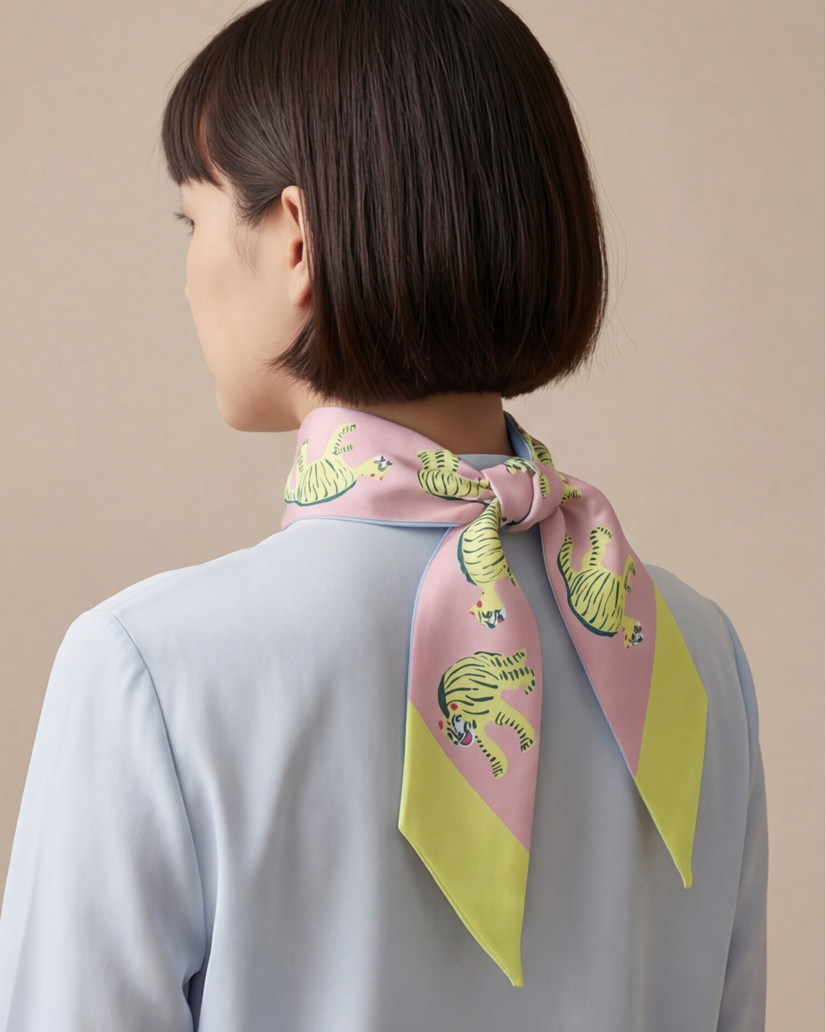 Twilly scarf worn at the neck, pastel blue and pink with green tiger print and ends