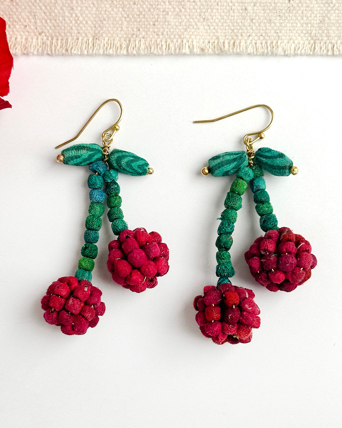 Pair of teal and red bead drop earrings with gold hooks and berry pom-poms.