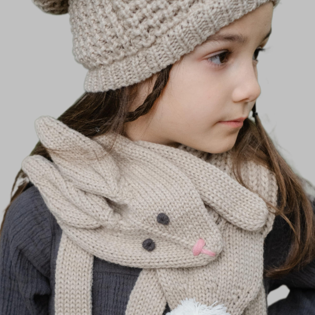 Oat beige rabbit scarf worn around a child's neck, showing its face and floppy ears