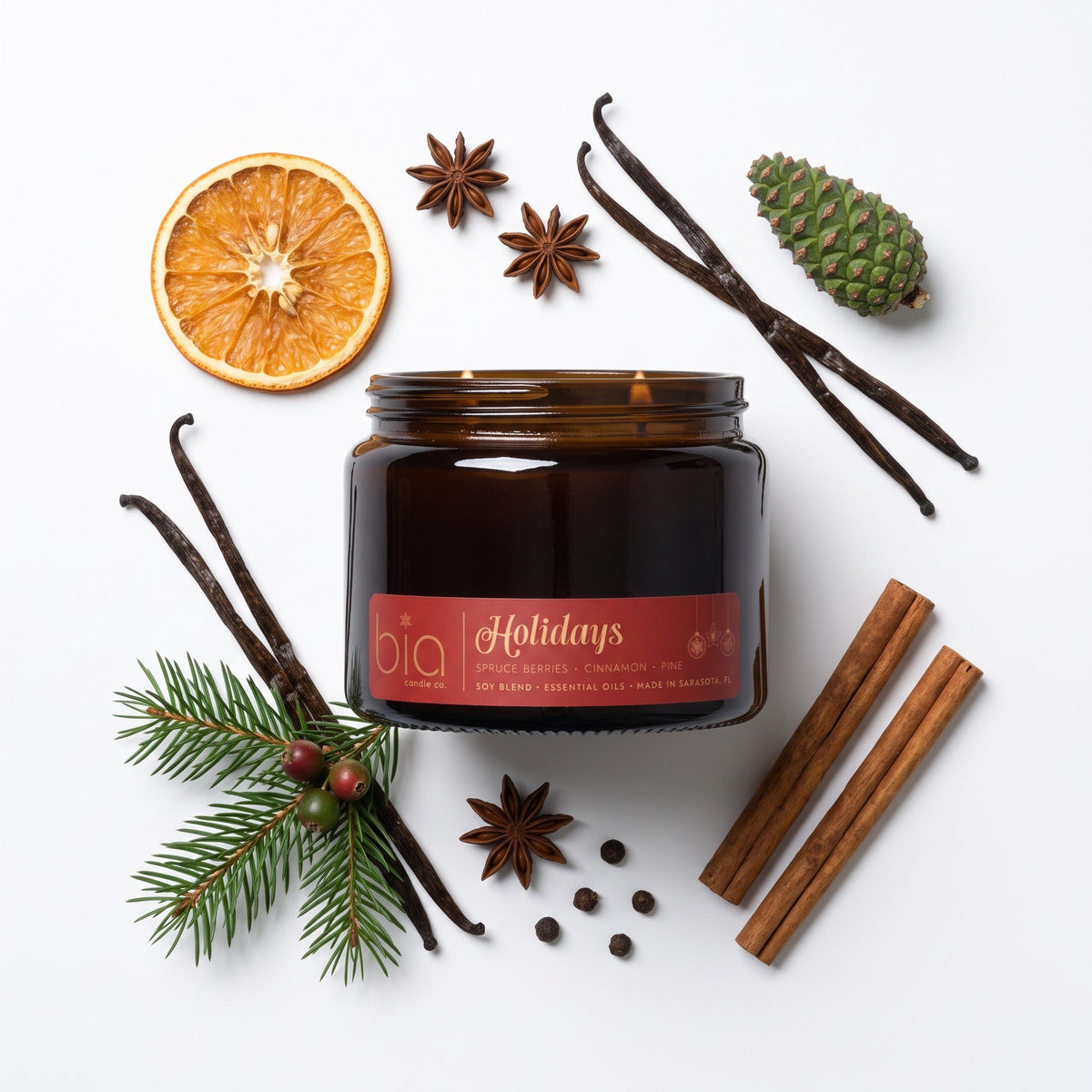 Amber candle jar with label, with orange slice, vanilla pods, and spices around.