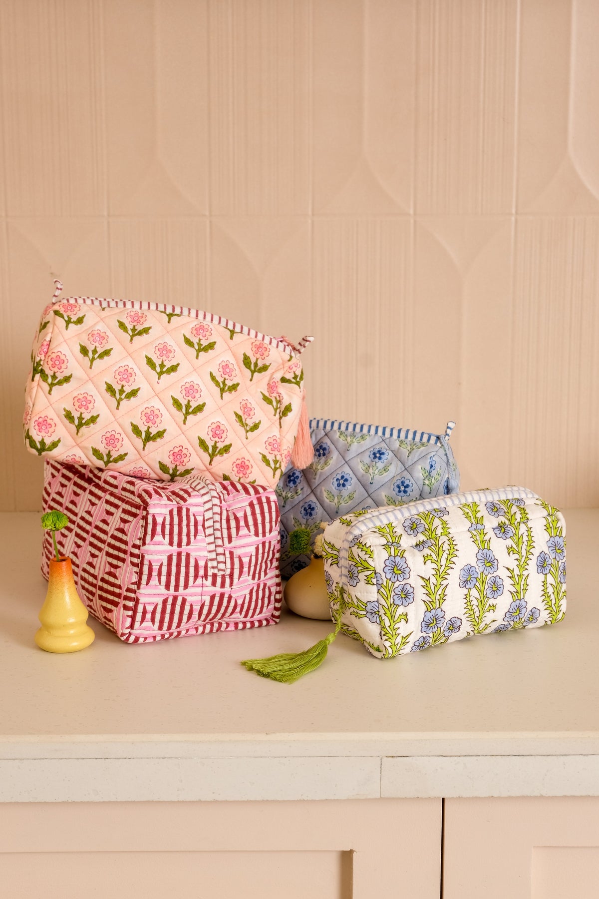 Blue floral blockprint zip pouch with green tassel, shown in front of other bags.