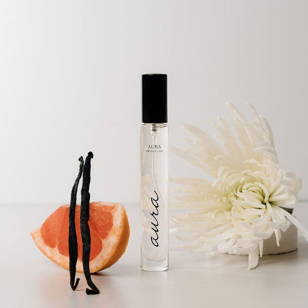 AURA perfume travel spray bottle with grapefruit slice and white flower blossoms nearby