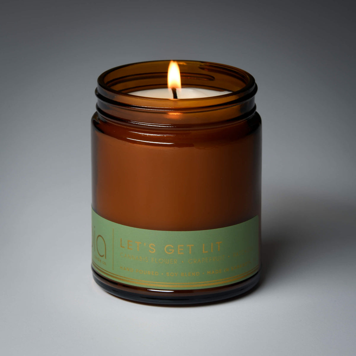 Amber jar candle with lit wick and green label on the front
