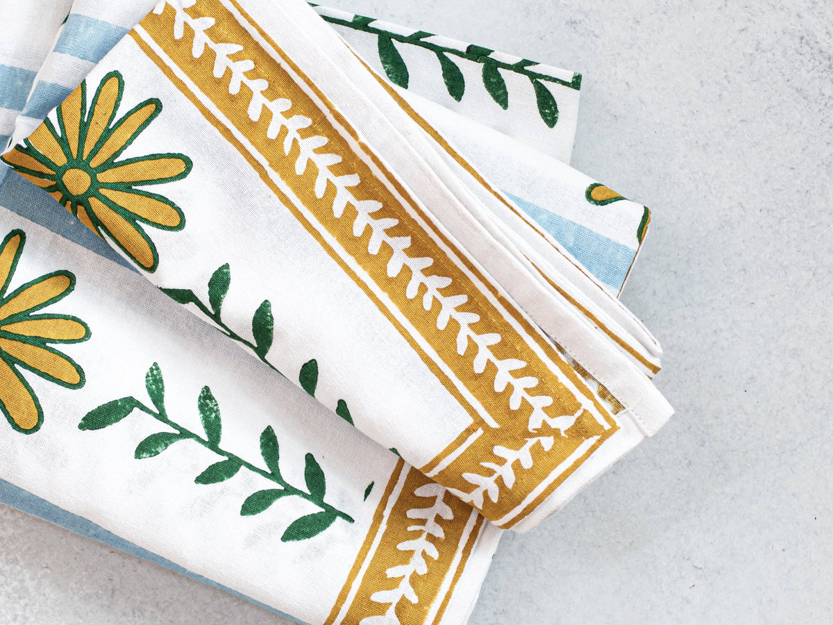 Table throw corner detail with blue stripes, green leaves, and mustard border stitching.