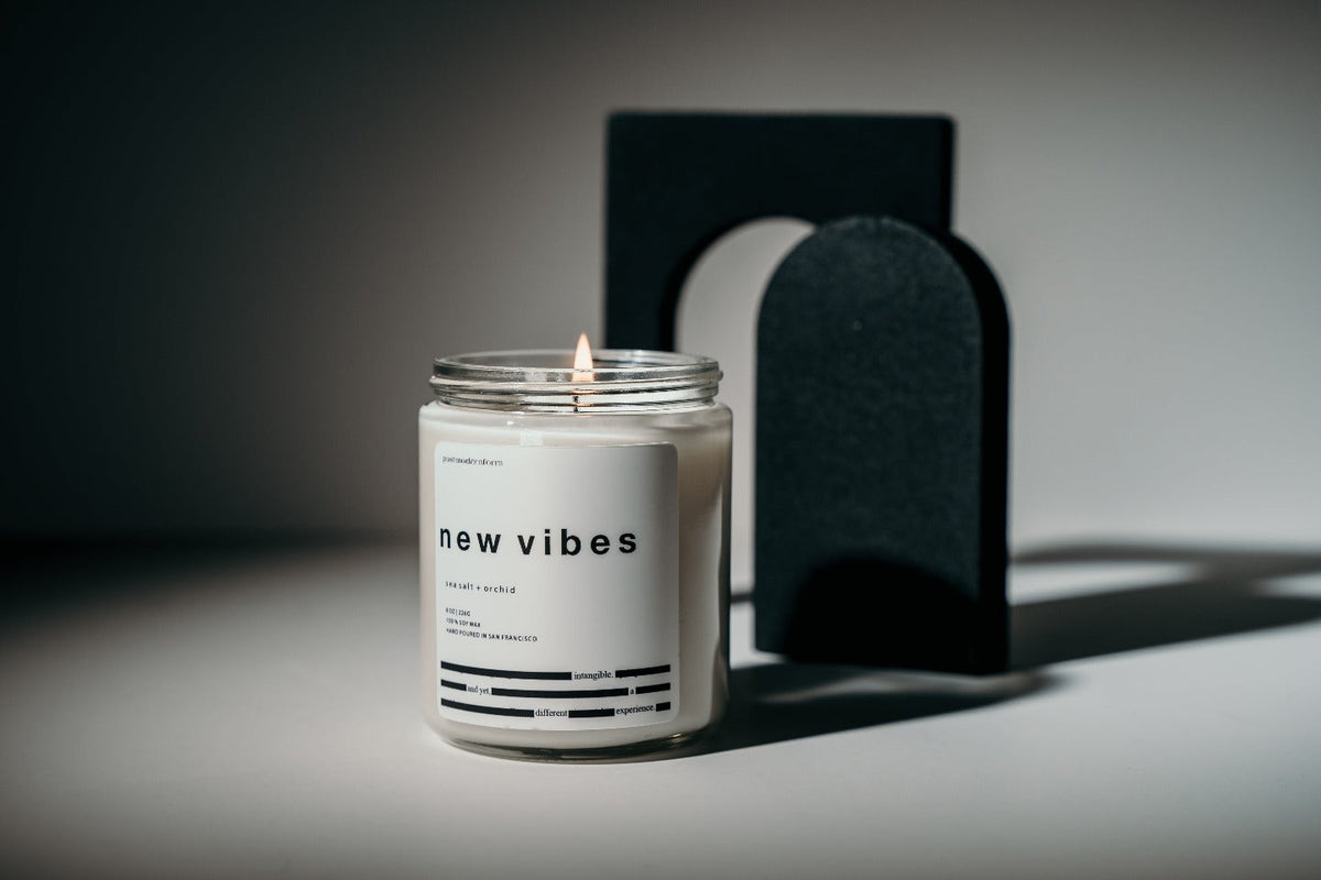 Candle in frosted glass jar with black lid; small flame visible above label