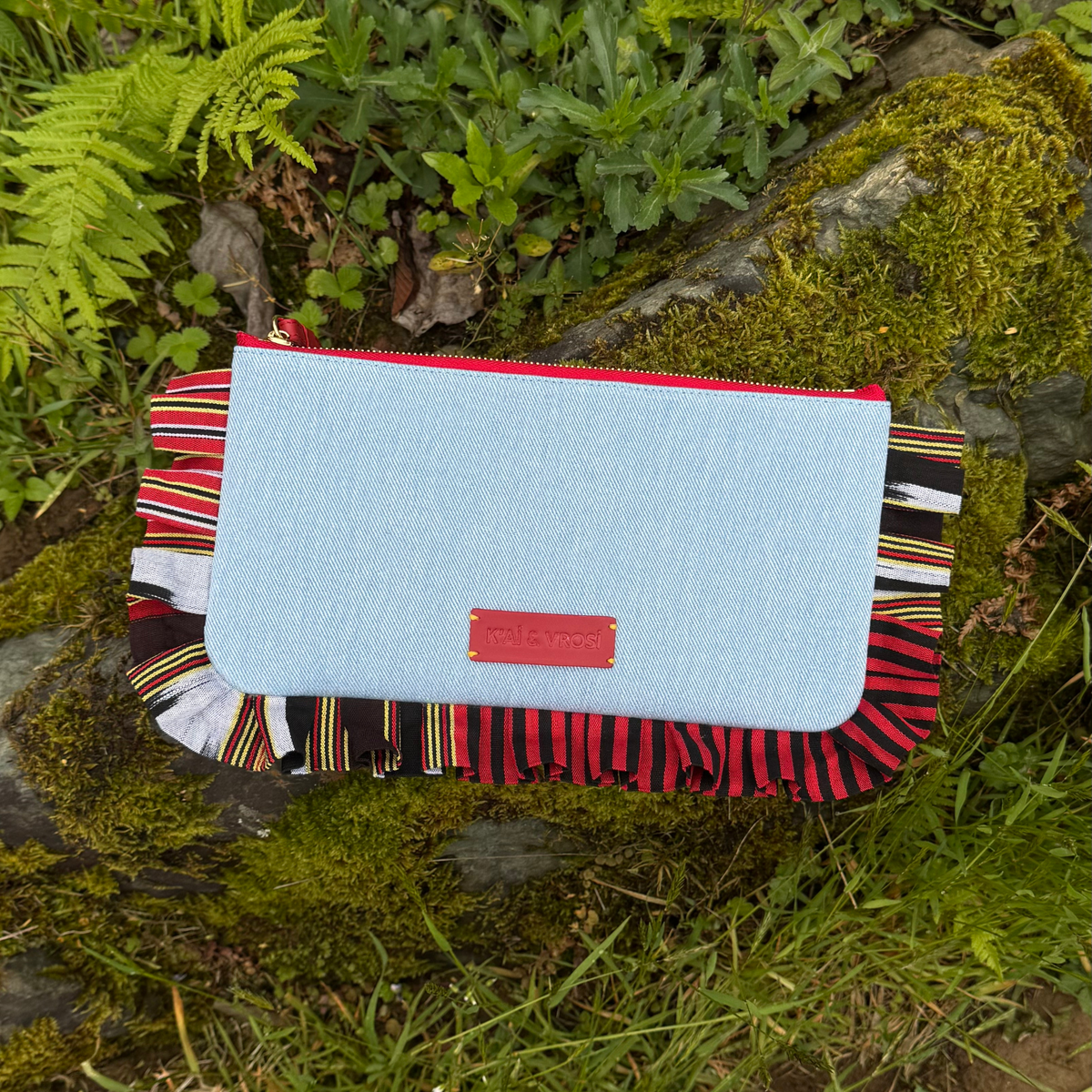 Light blue denim clutch on textured background with fringed striped trim and red trim