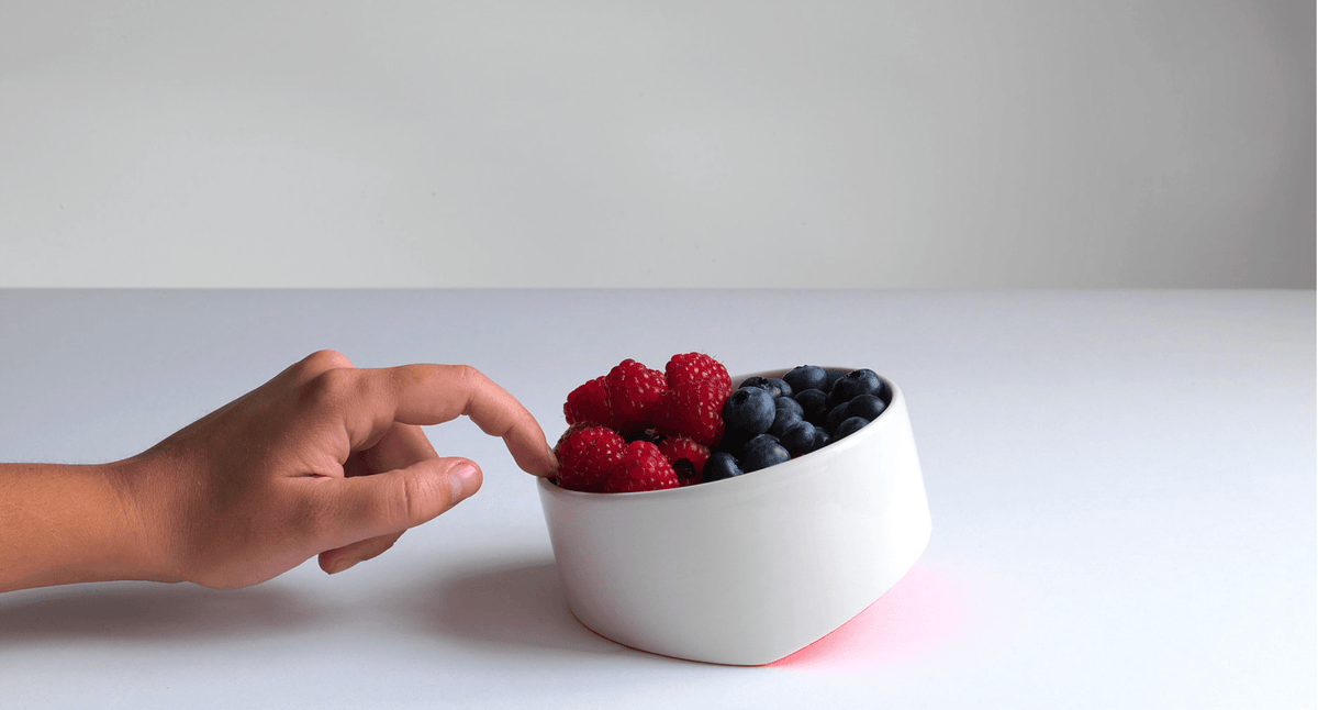 Ceramic bowl with berries, shown with a hand placing fruit