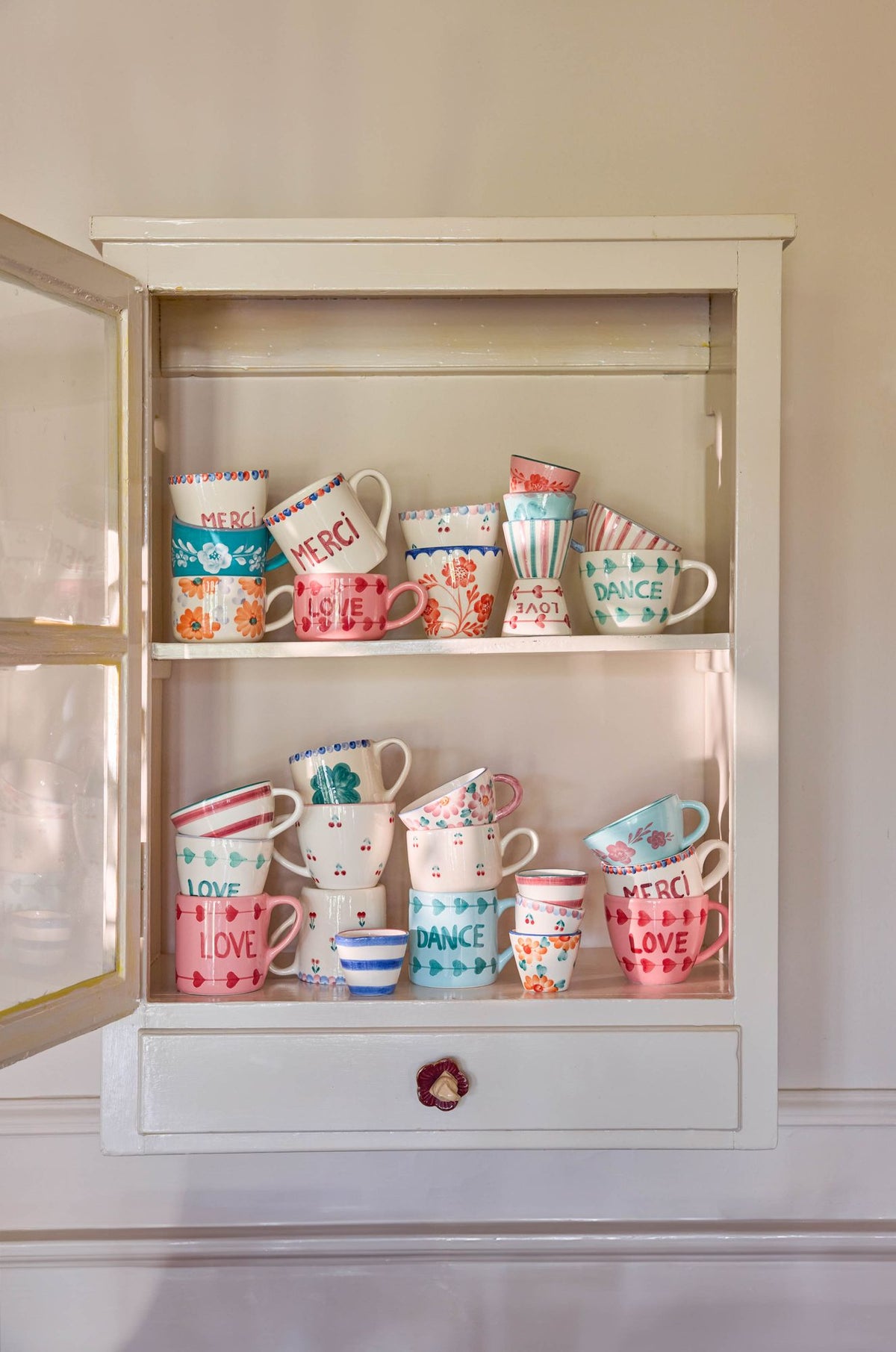 Ceramic cappuccino cups with orange floral designs displayed in a cabinet