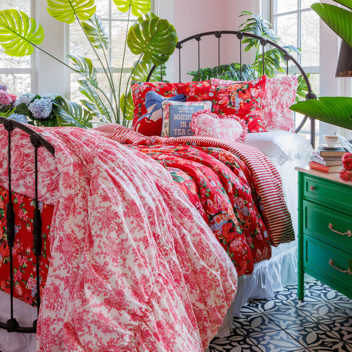 Red floral bedding with an embroidered pillow reading “She’s Whiskey in a Tea Cup”