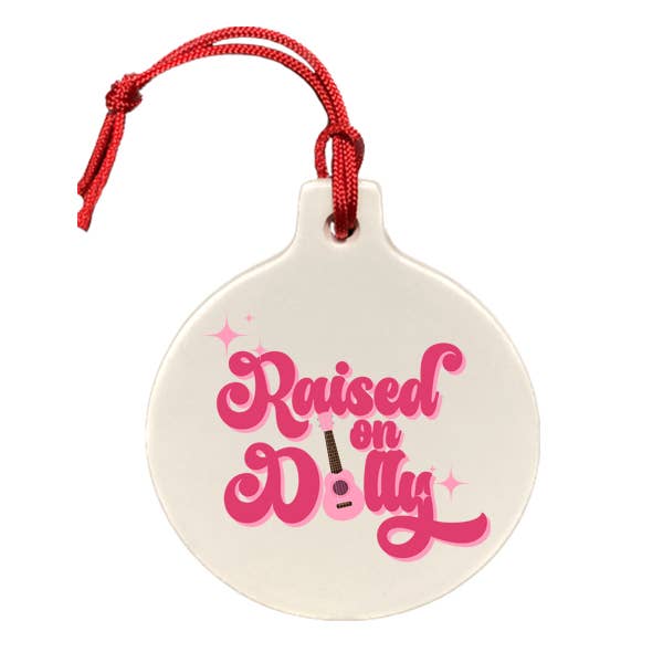 Ceramic ornament with red hanging cord and pink “Raised on Dolly” lettering