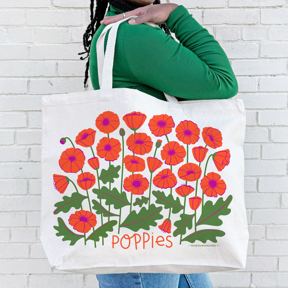 White canvas tote bag held over shoulder, red-orange poppy floral print with “Poppies”.