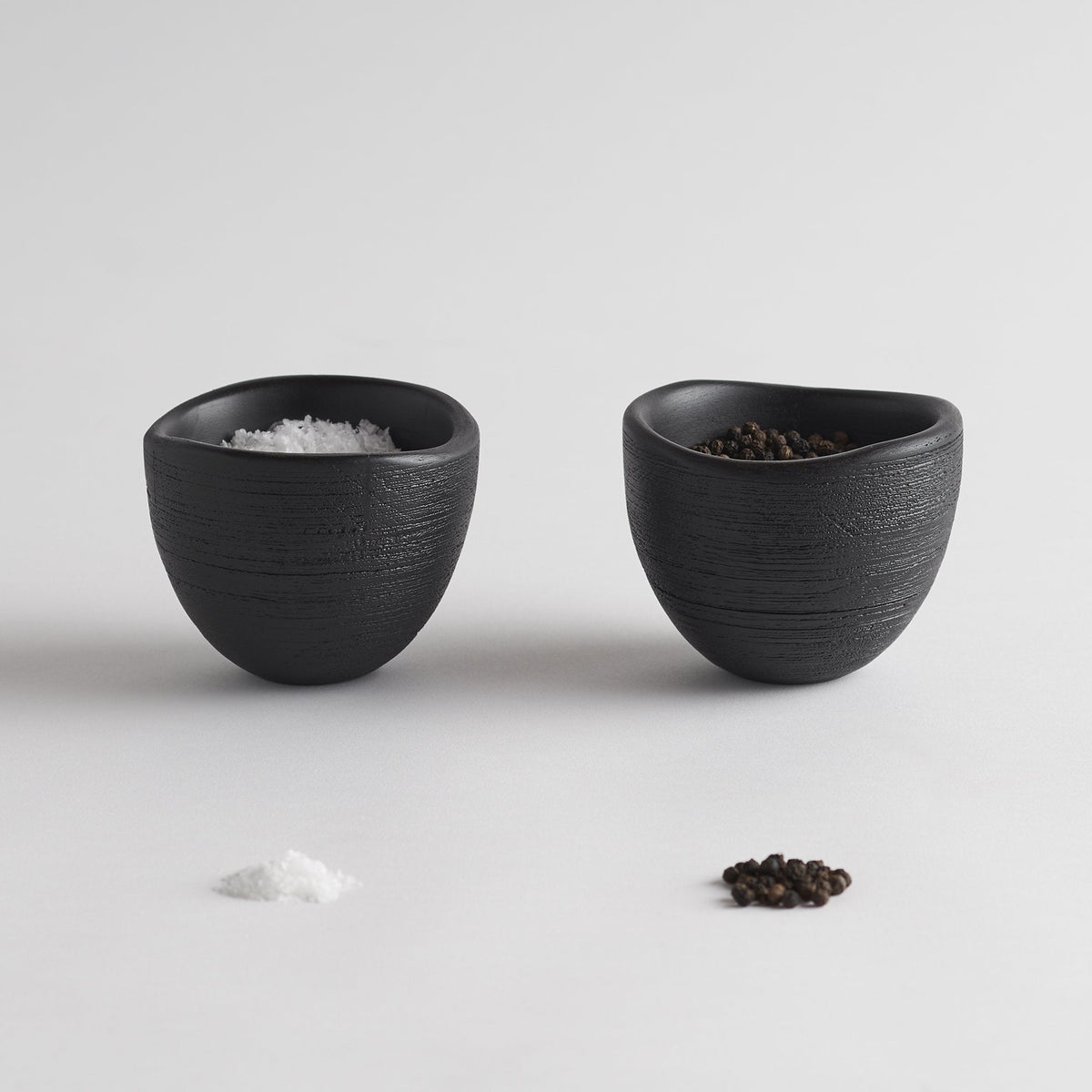 Set of 2 black textured bowls, one with salt and one with peppercorns