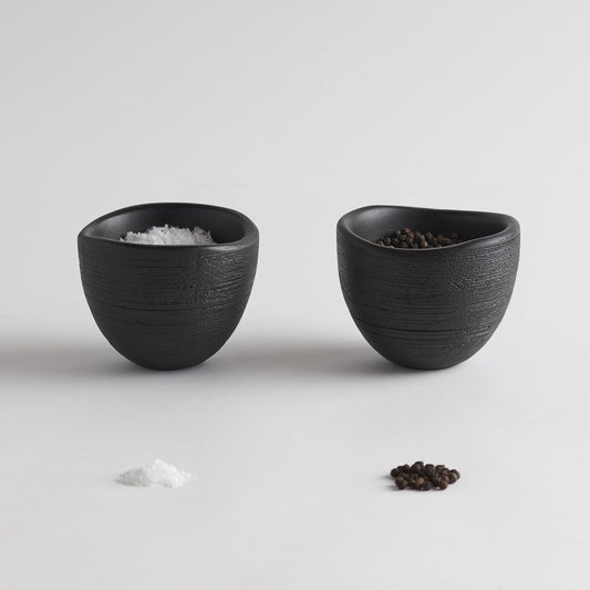 Set of 2 black textured bowls, one with salt and one with peppercorns