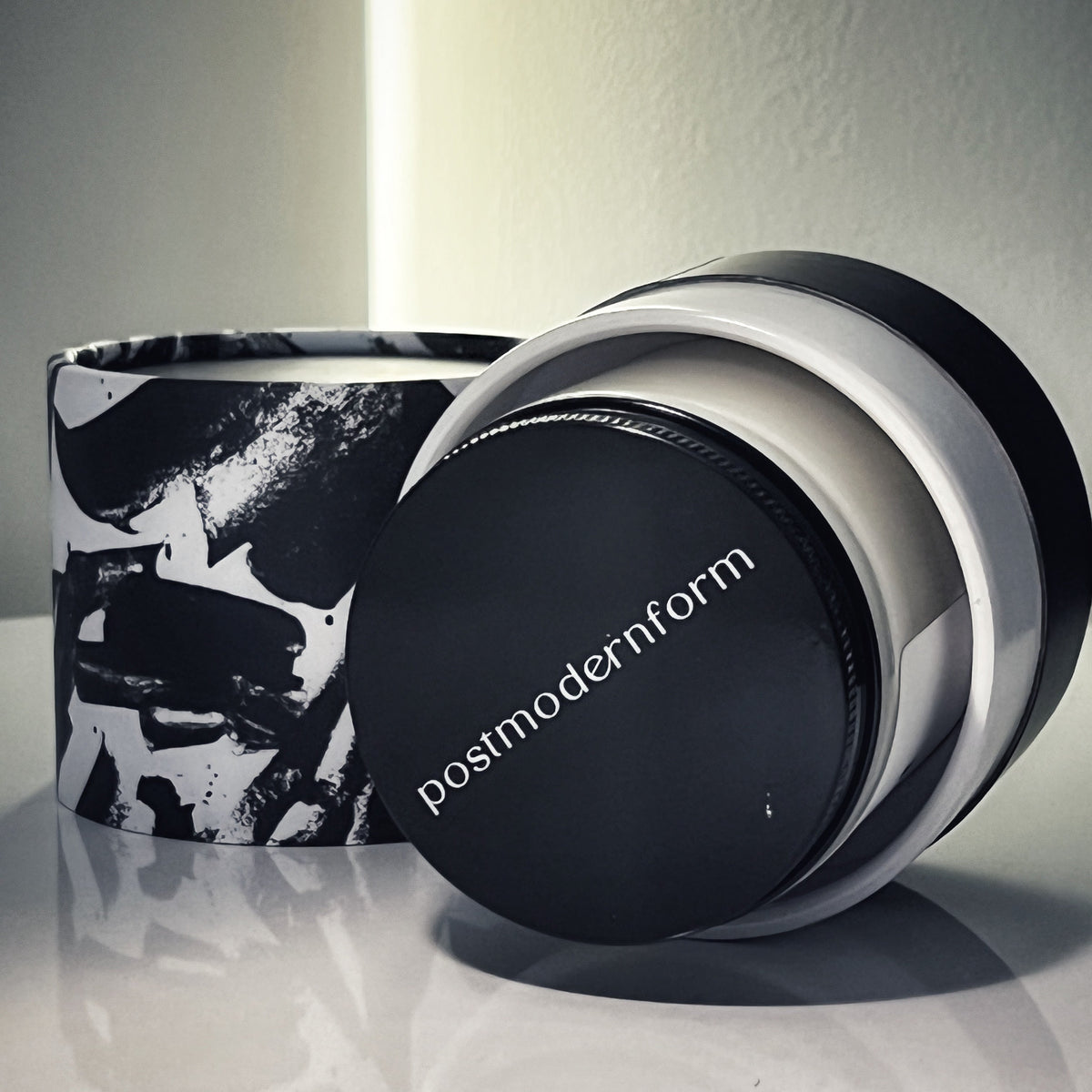 Black-lidded candle jar with postmodernform on lid beside matching black-and-white box