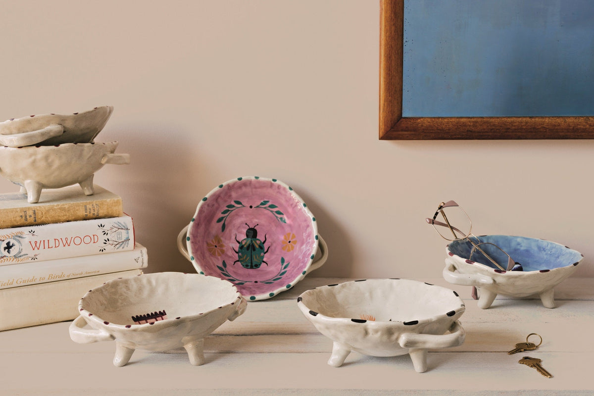Footed ceramic bowls with animal prints and beige tripod bases, including blue and pink