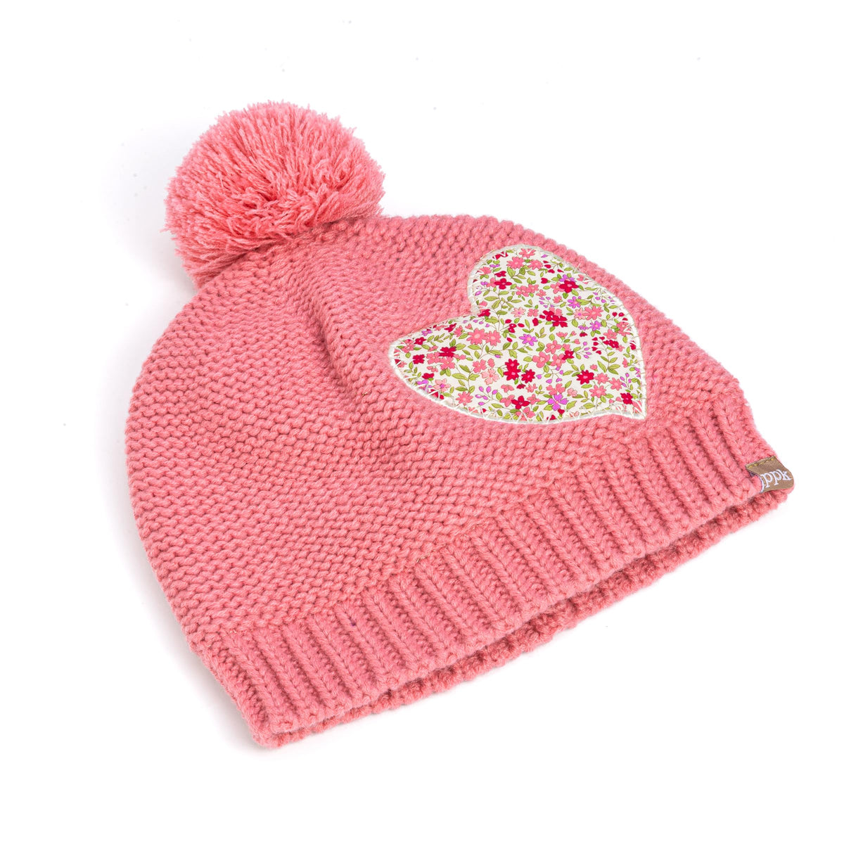 Angled view of coral pink knit beanie with pompom and floral heart applique