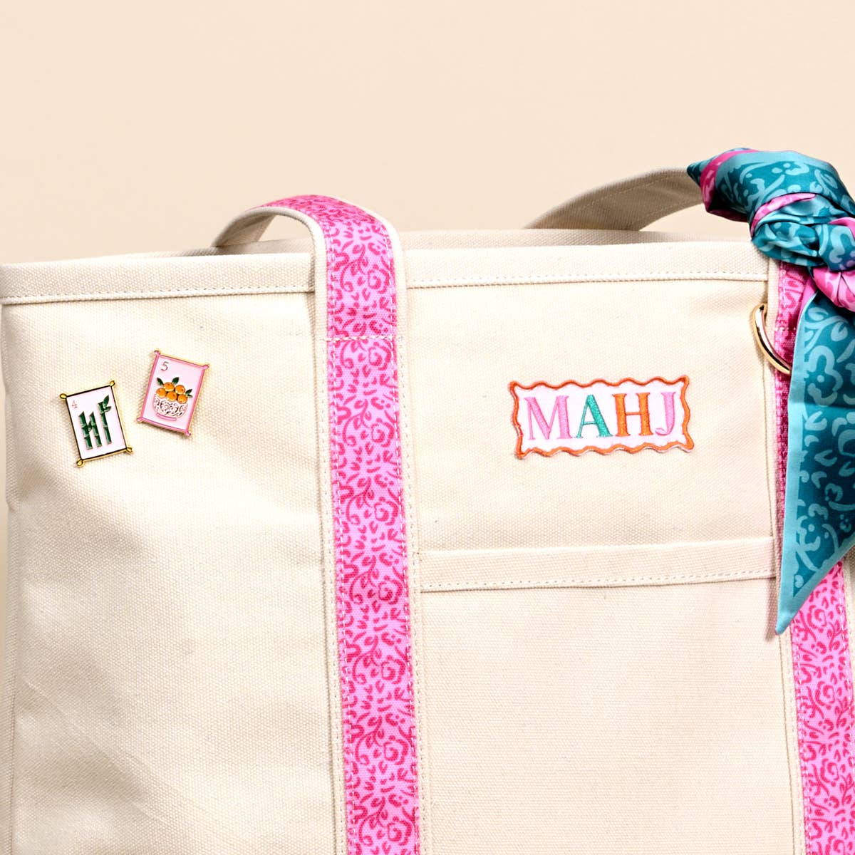 Cream canvas tote close-up with MAHI patch, pins, pink trim, and patterned ribbon bow
