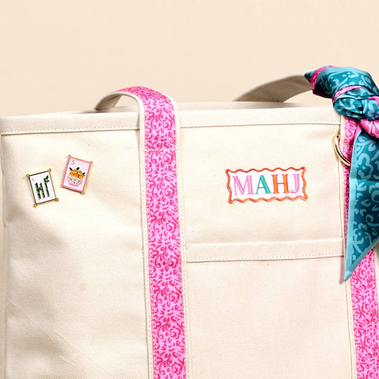 Cream canvas tote close-up with MAHI patch, pins, pink trim, and patterned ribbon bow