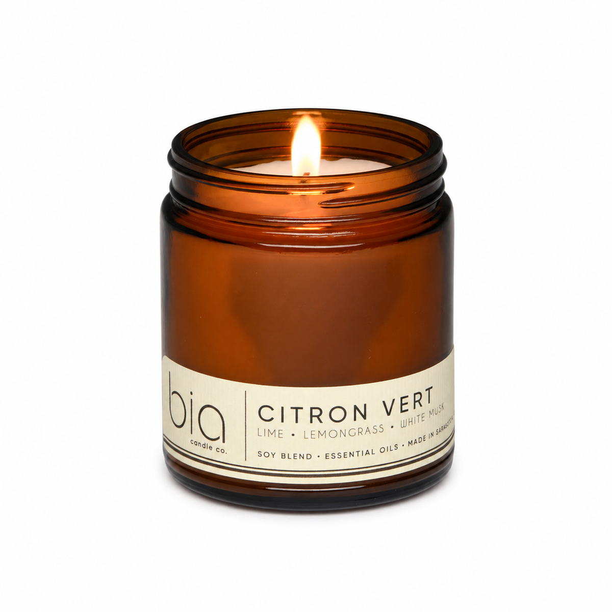 Amber glass soy blend candle jar with lit wick and cream Citron Vert label.