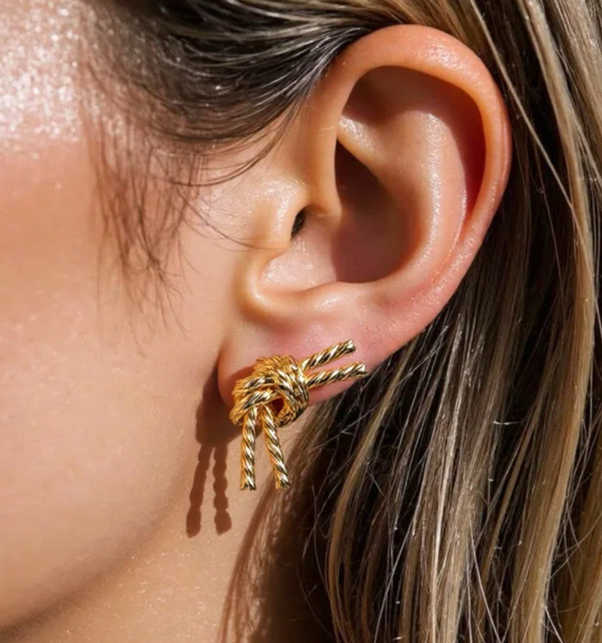 Gold-plated rope knot stud earrings, worn on ear in close-up
