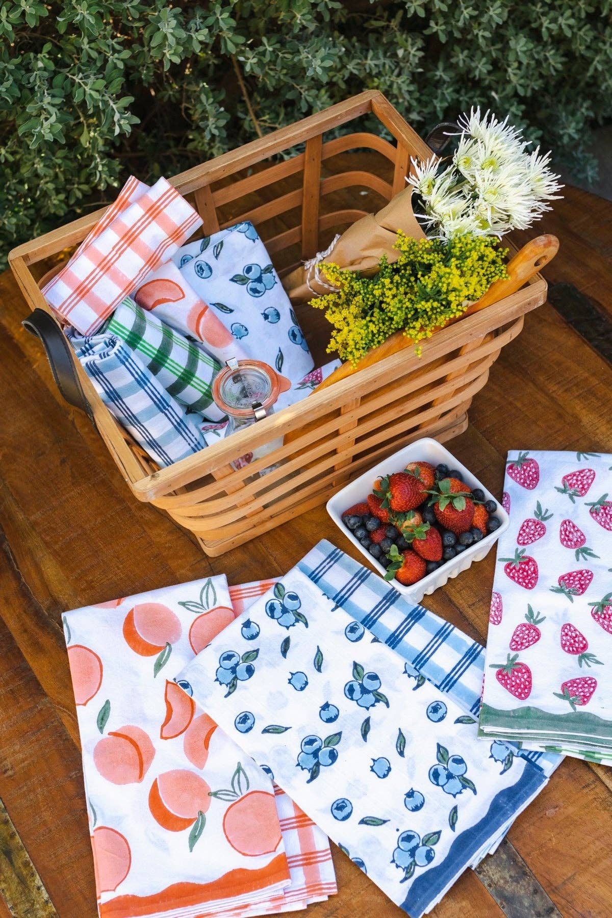 Blueberry tea towel with blue berry print and blue plaid edge, in a wooden basket