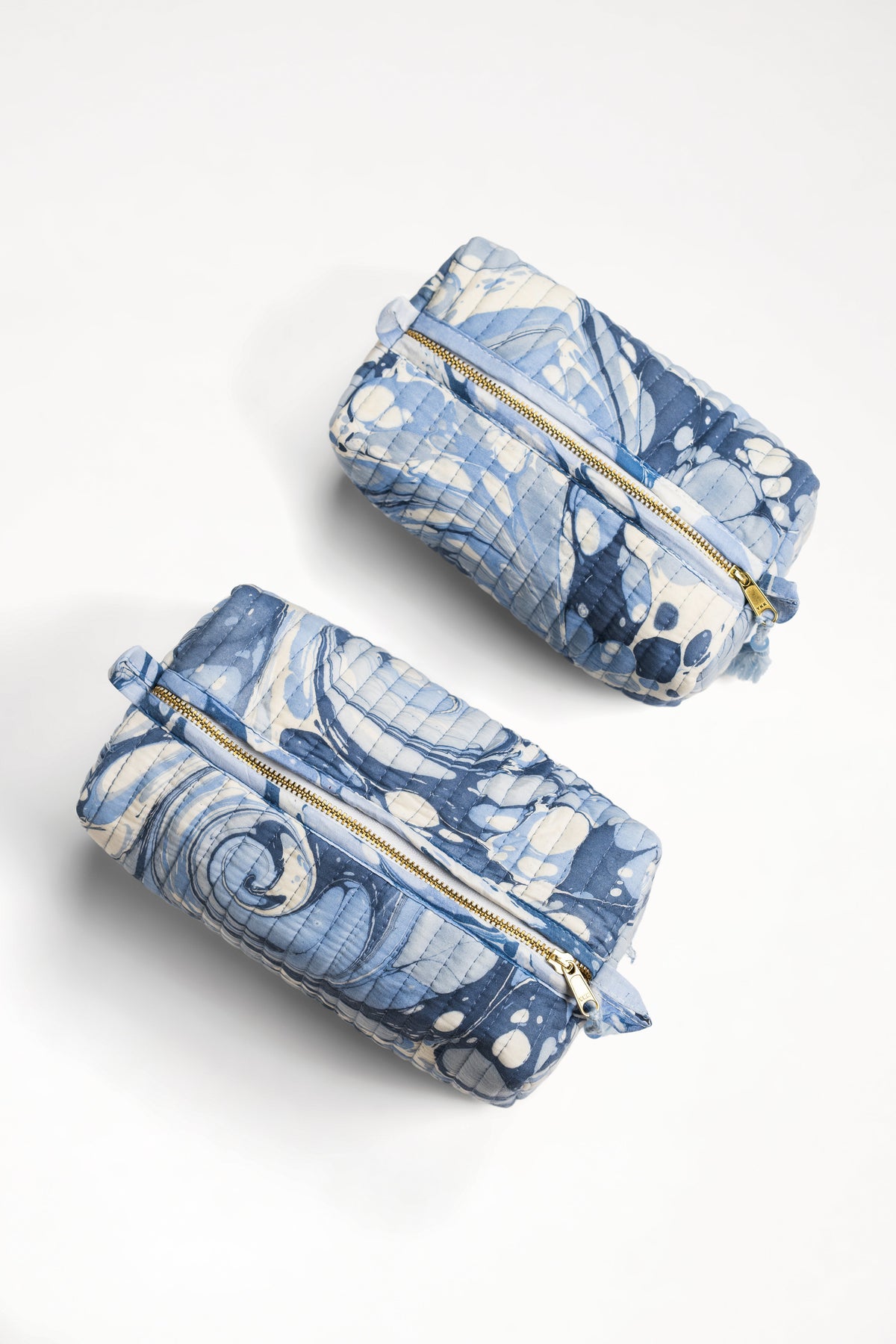 Two blue zip cosmetic pouches with gold zipper and tied corner bows, angled view