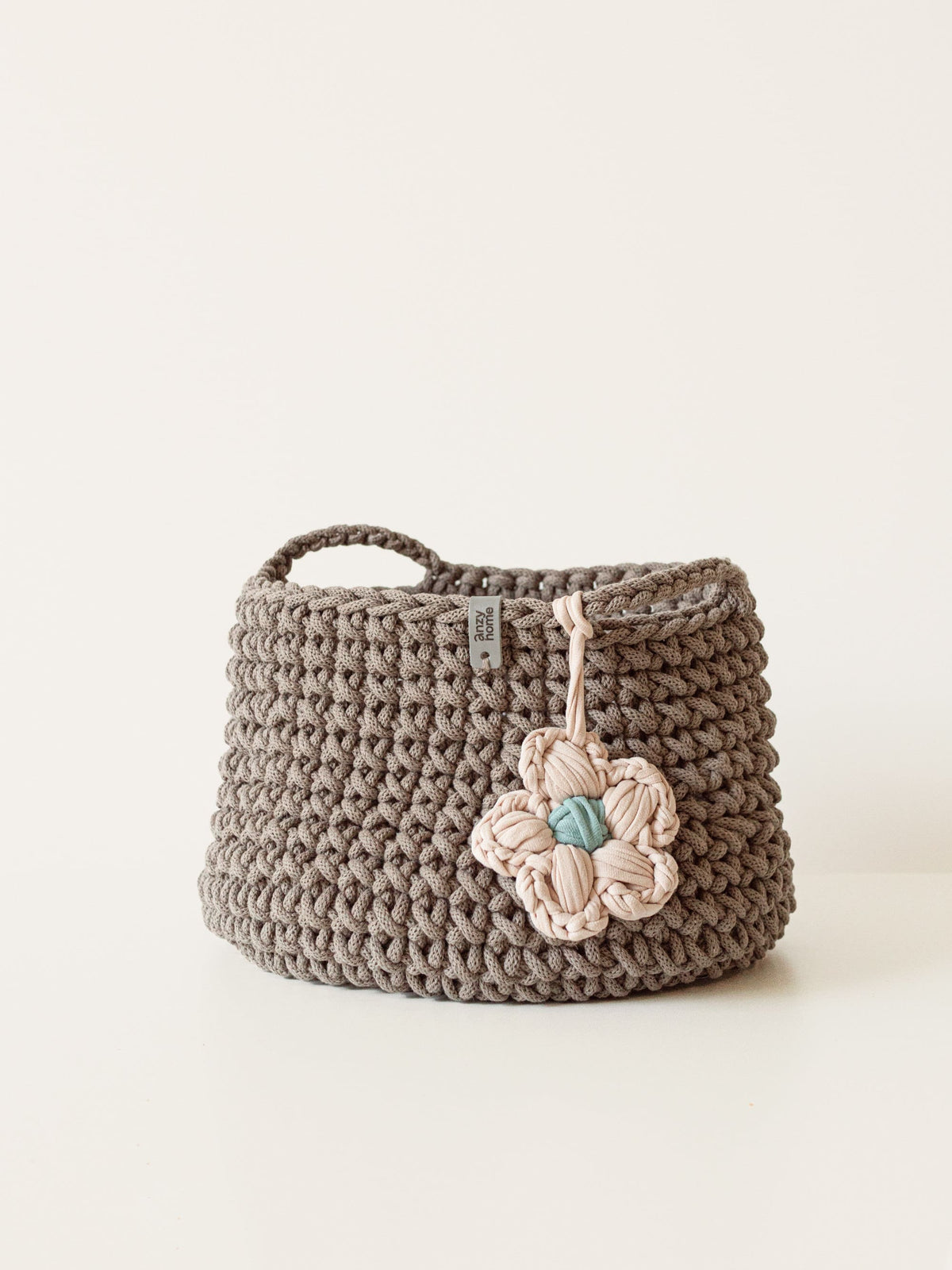 Gray crochet storage basket with beige flower applique and braided carry handles