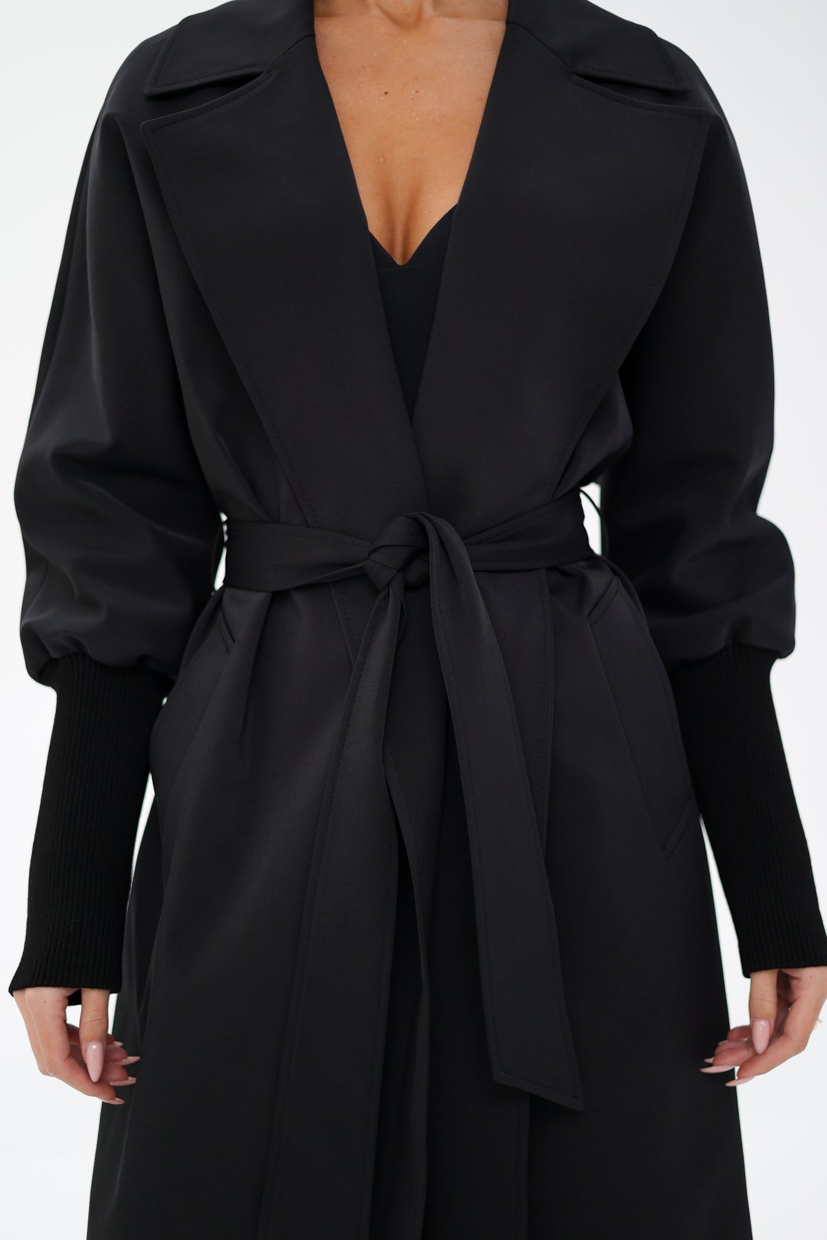 Black trench coat front detail with wide lapels, tie belt, and ribbed cuffs