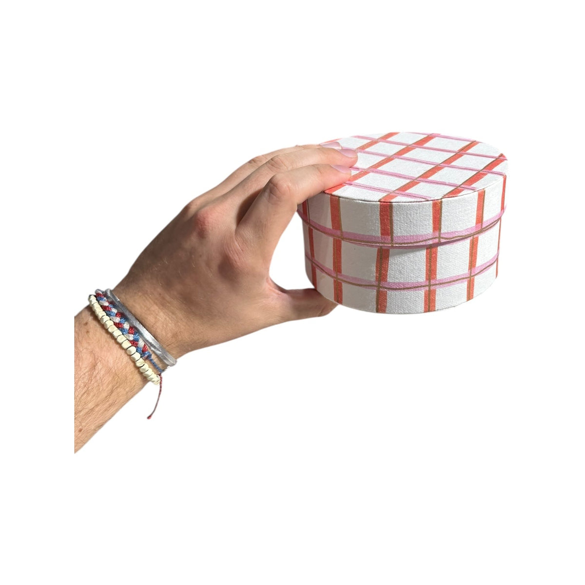 Hand holding a round handmade recycled paper gift box with red plaid stripes and striped lid.