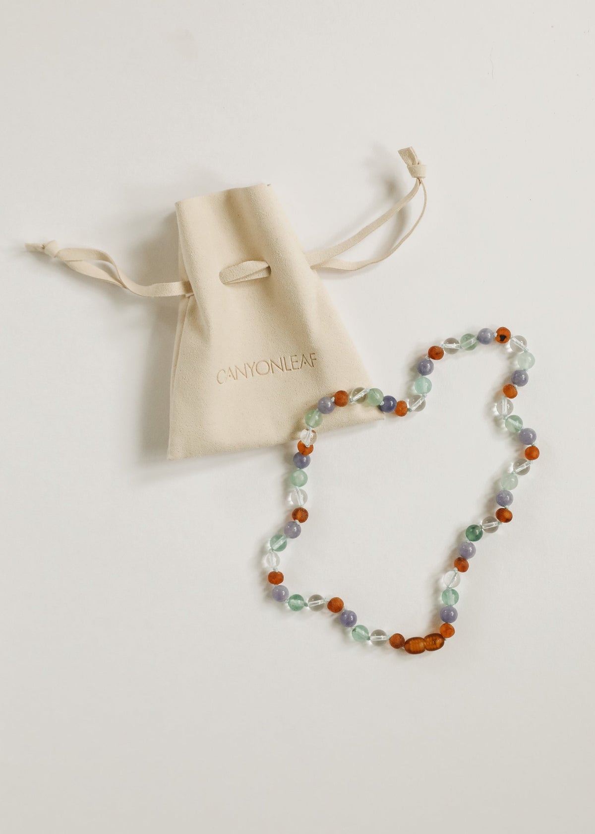 Beaded gemstone necklace with orange amber, mint, and lilac beads beside fabric gift pouch