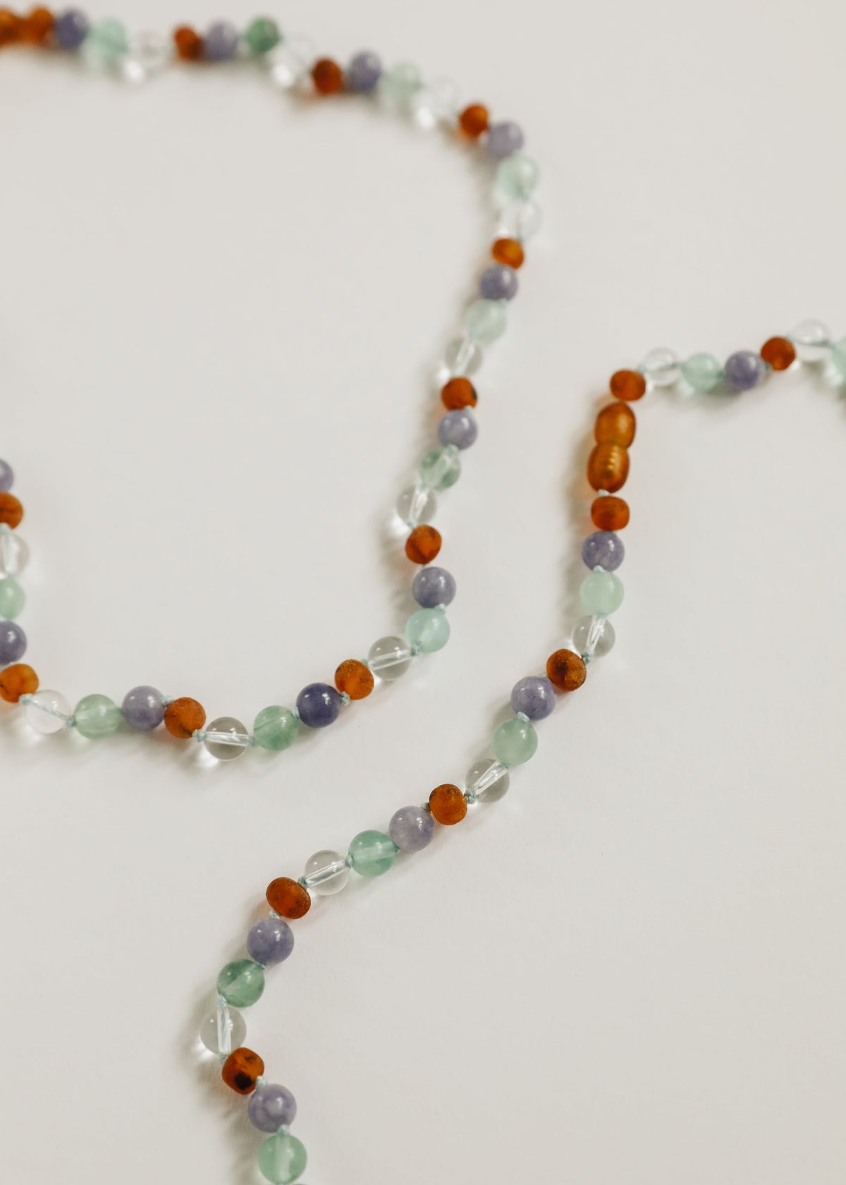 Close-up beaded gemstone necklace strand with orange amber, mint, and lilac beads