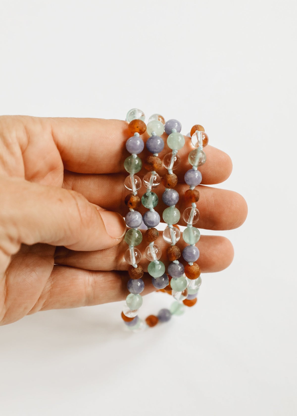Beaded gemstone necklace strand held in hand with orange amber, mint, and lilac beads