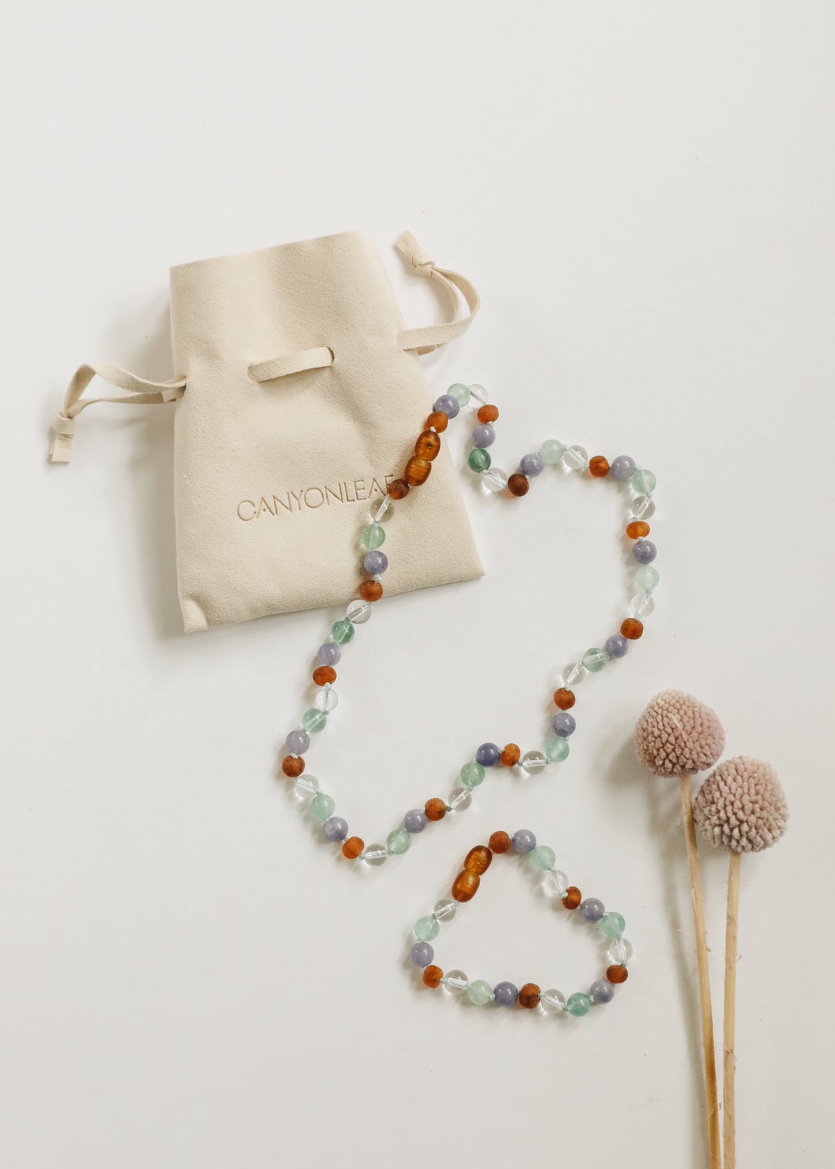 Beaded gemstone necklace with orange amber, mint, and lilac beads near beige pom-poms