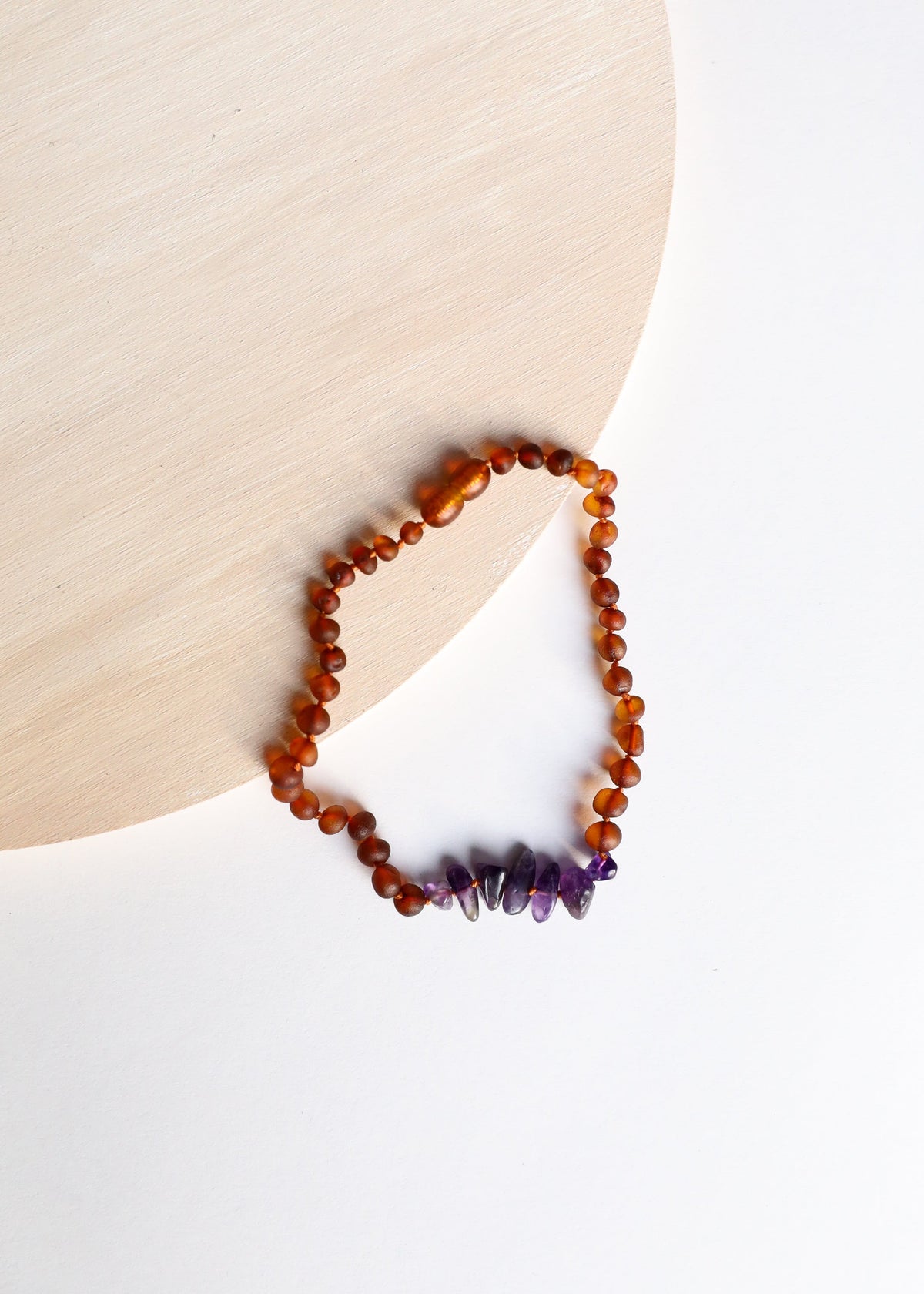 Amber beaded heart-shaped necklace with purple amethyst points near the bottom.