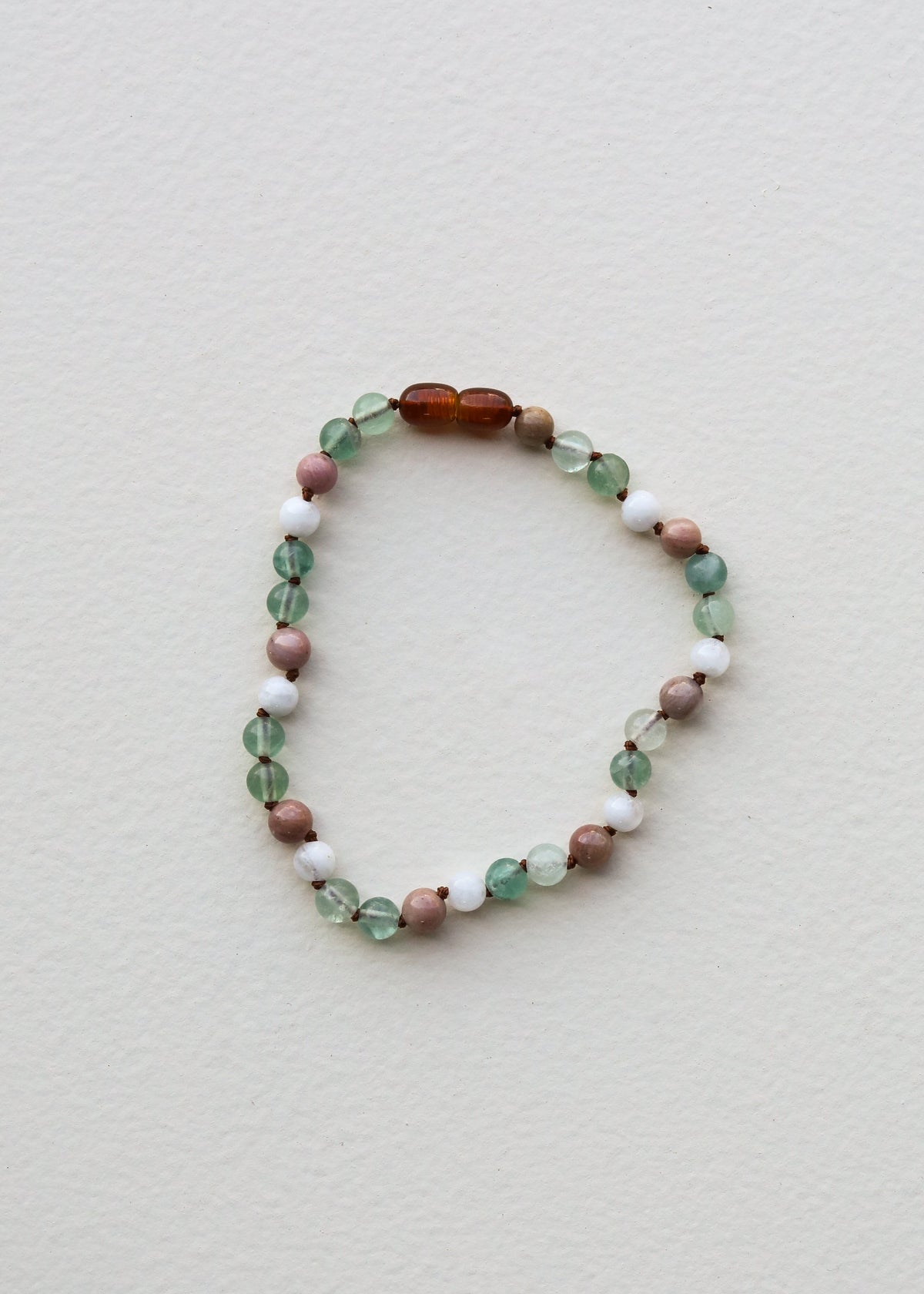 Gemstone beaded bracelet with green oval beads, pink accents, and an amber center bead