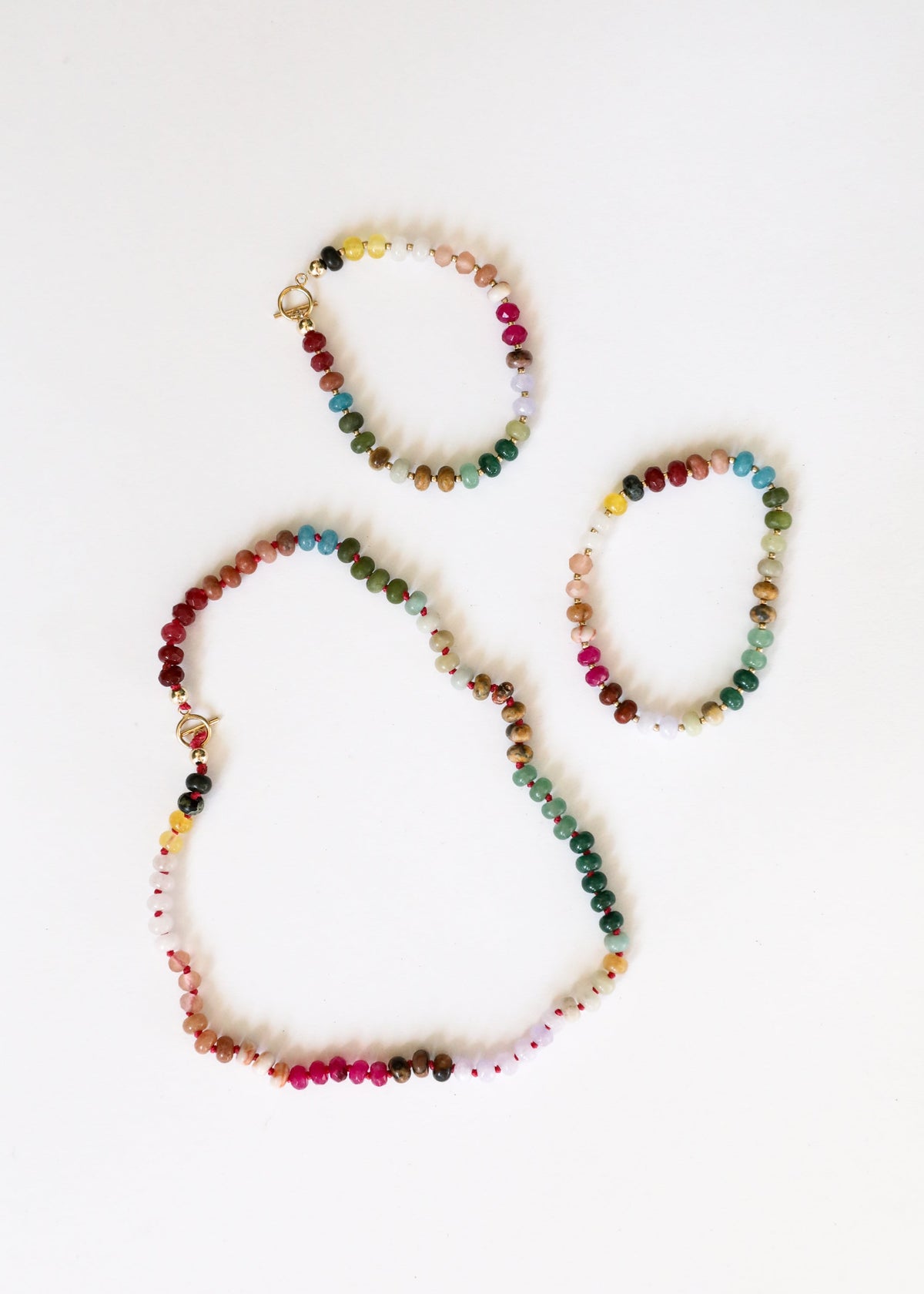 Set of multi-color gemstone beaded necklaces with gold toggle clasps, flat lay.