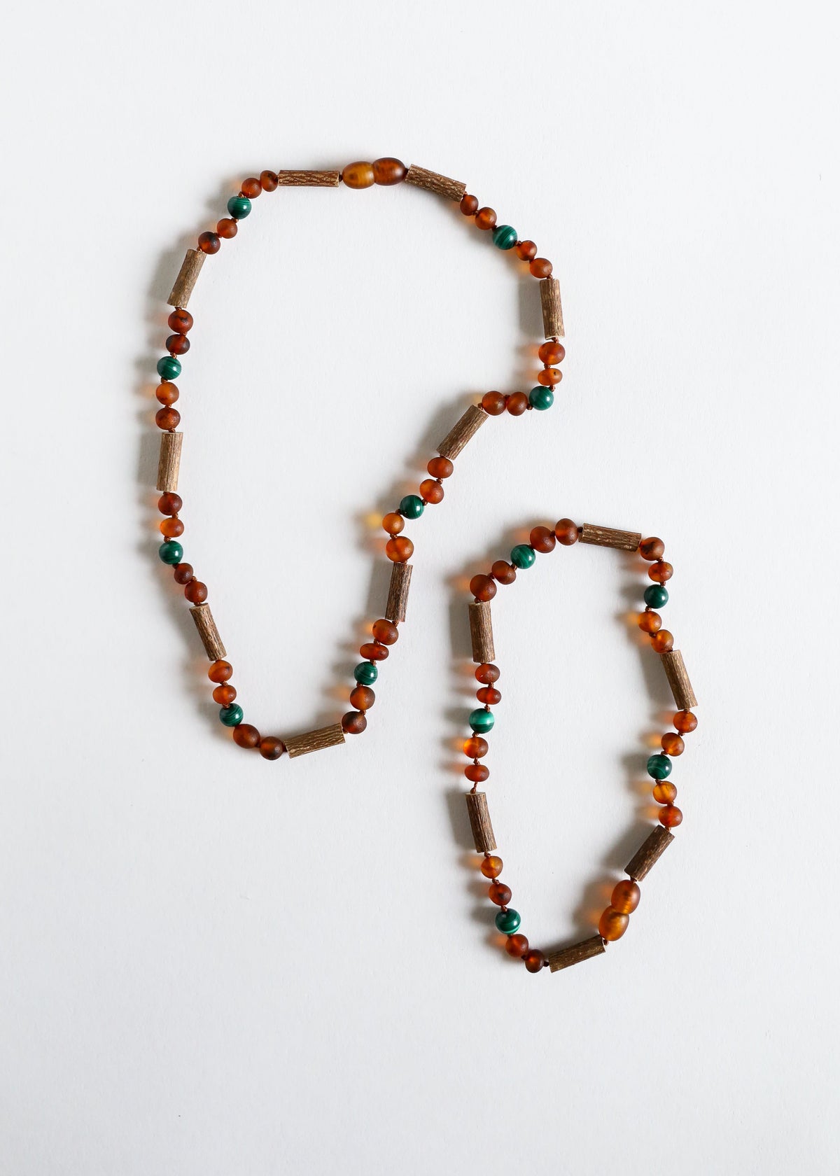 Two amber and malachite beaded necklaces laid flat, with teal and dark brown beads
