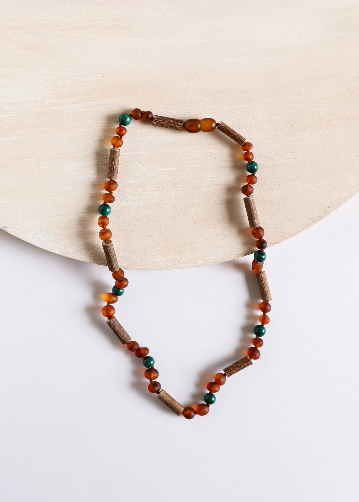 Amber and malachite beaded necklace on light background, round amber beads with teal dots