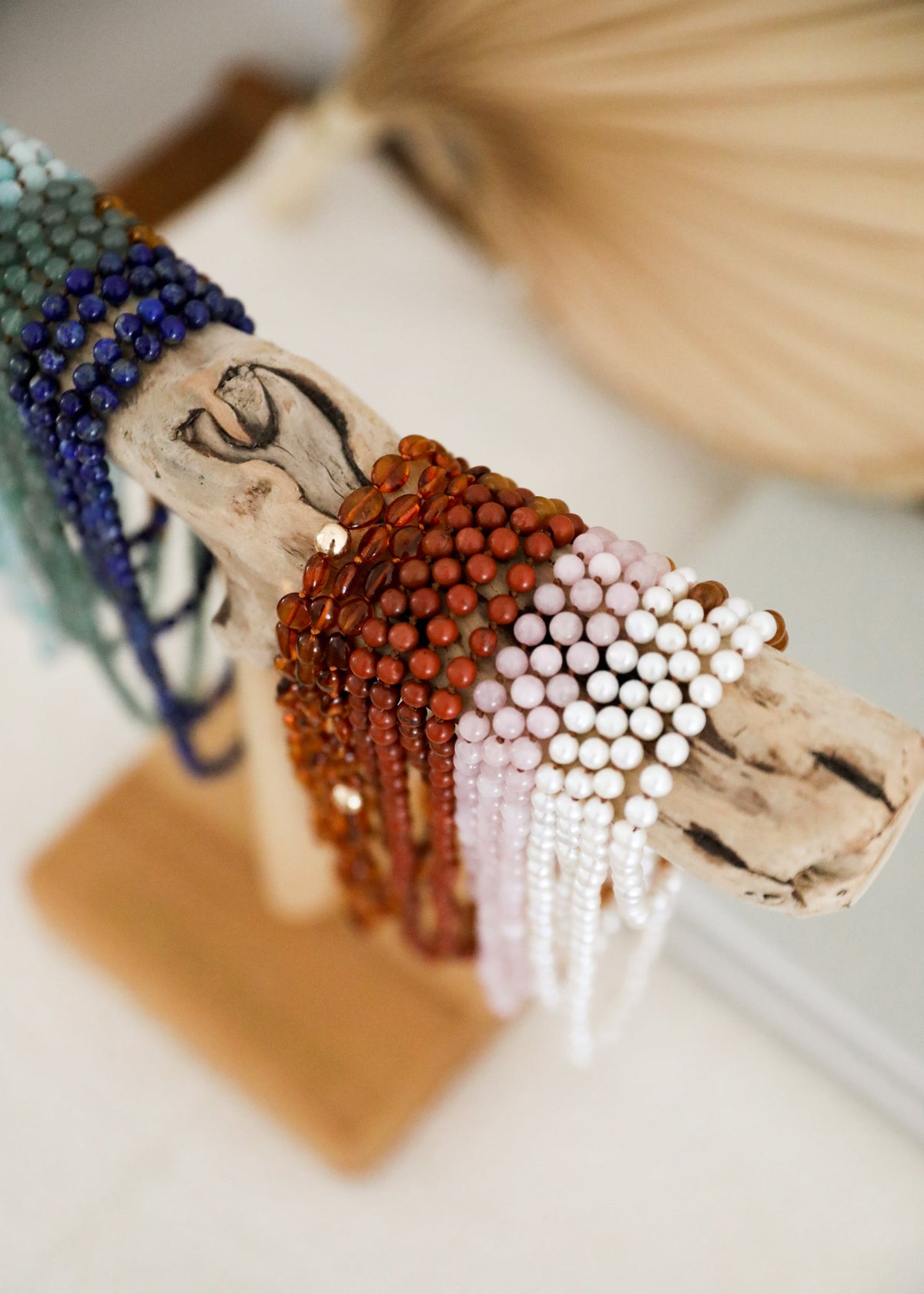 Closeup of beaded bracelet: blue, orange, and white pearl strands on wooden display form