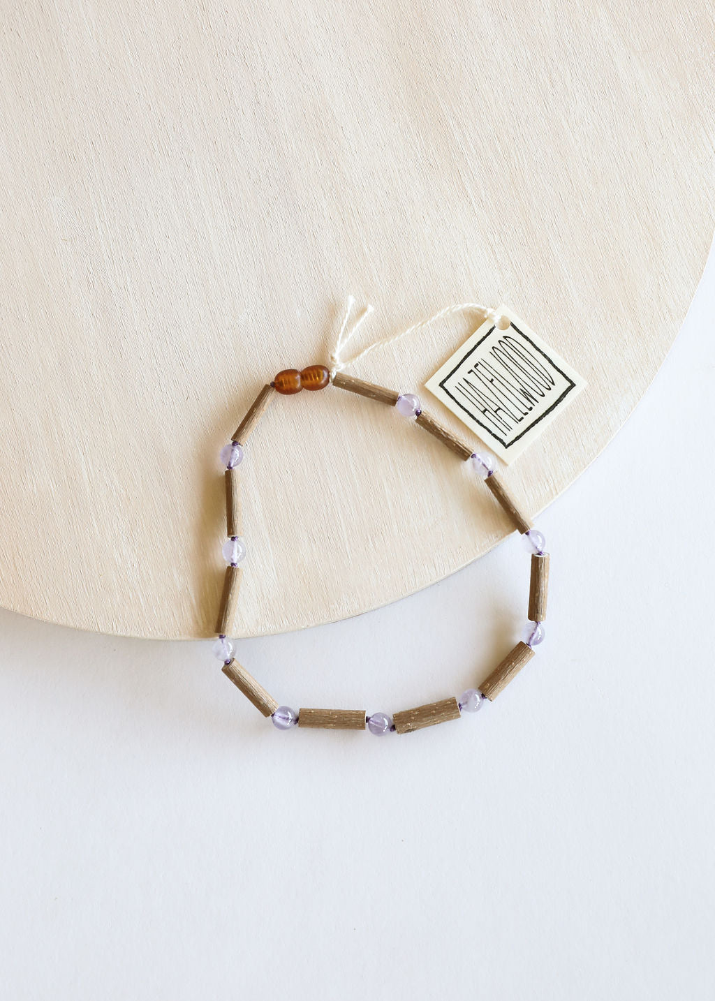 Beaded necklace with clasp and small tag; light brown beads, lavender accents, amber bead