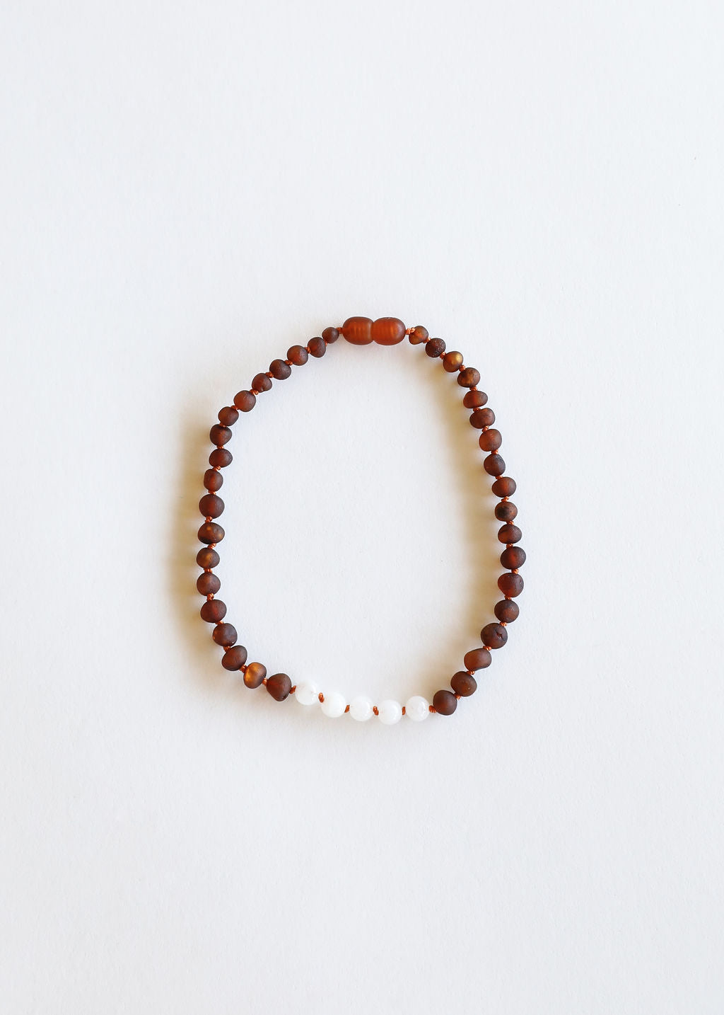 Brown amber bead necklace with small white moonstone beads, laid flat