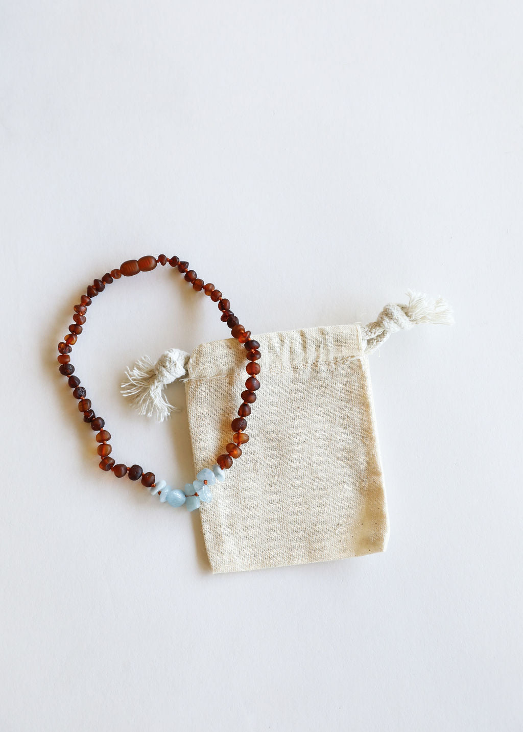 Amber-brown bead necklace with light blue stone and white tassel ends