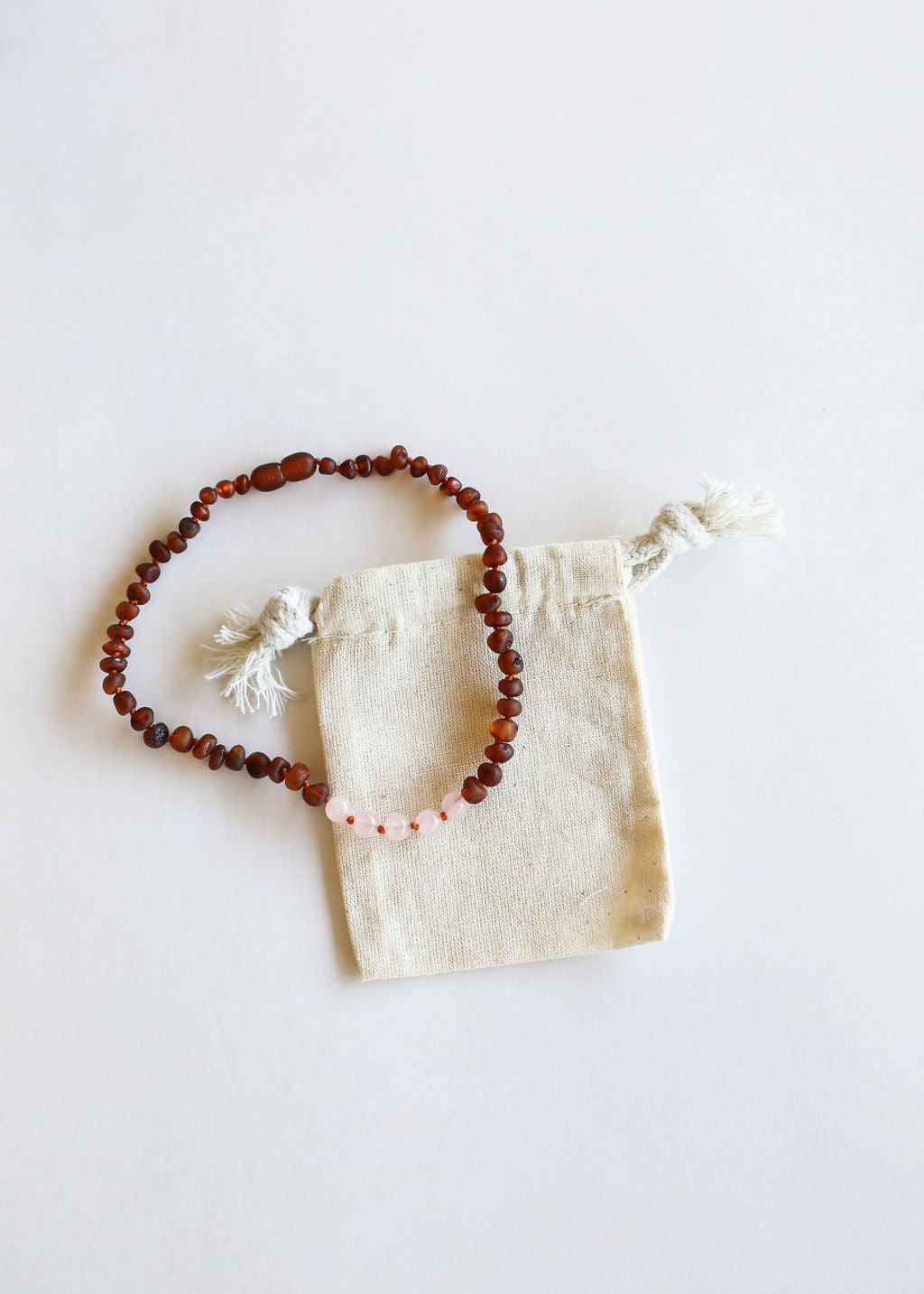 Amber bead necklace with rose quartz teardrops, shown on linen pouch