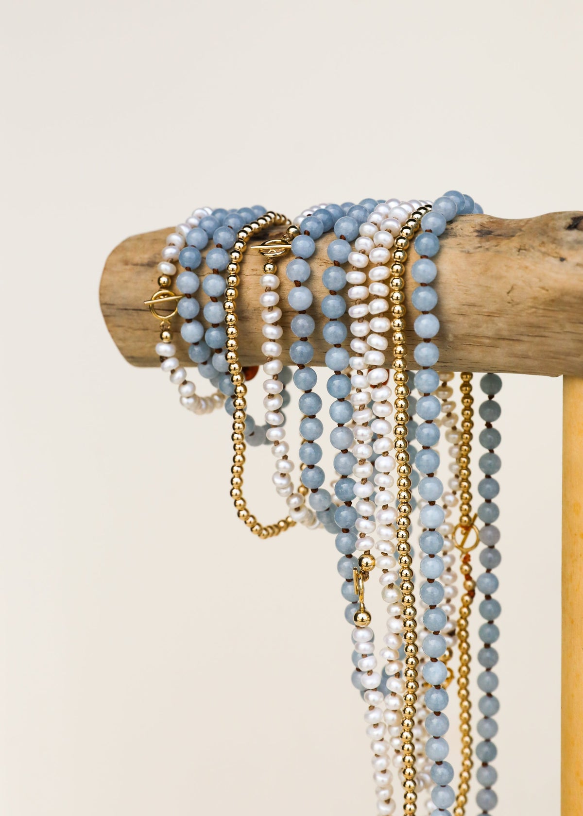 Stacked aquamarine and white pearl bracelets with gold chain and charms
