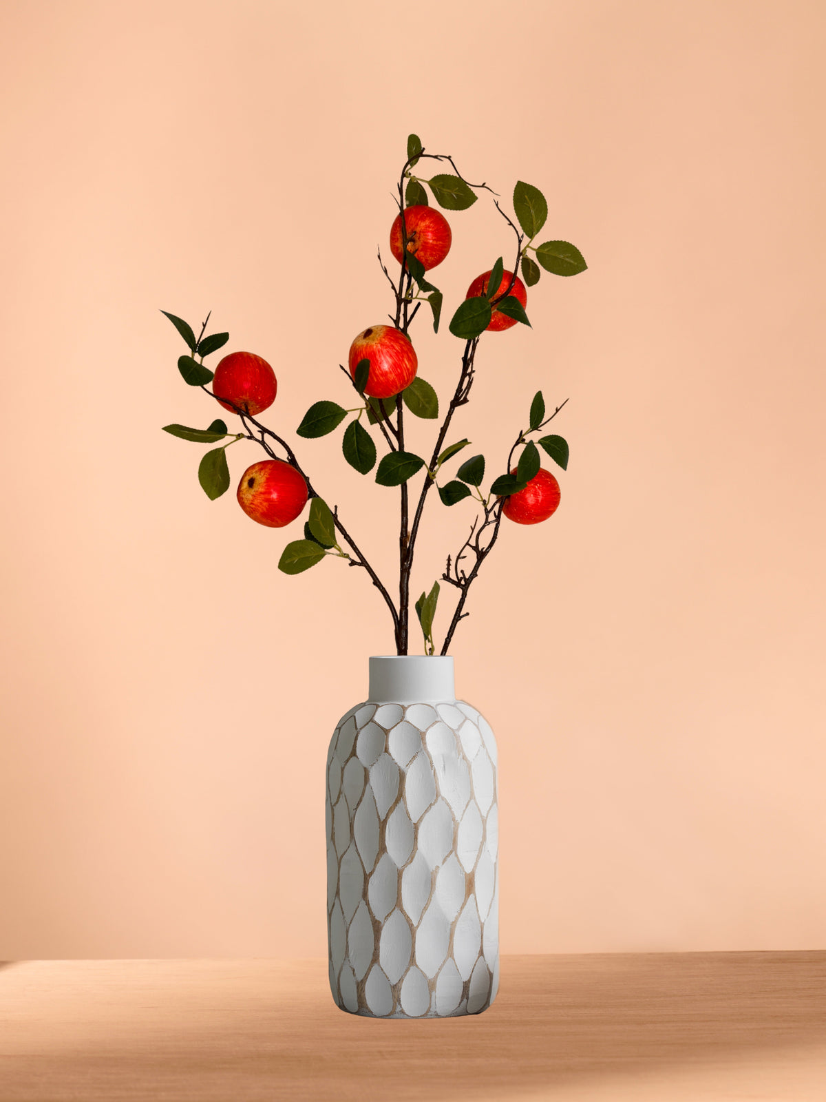 Artificial apple stems with red apples and green leaves in a textured ceramic vase