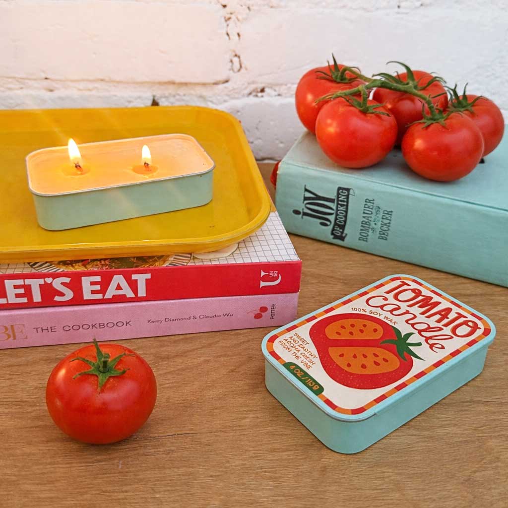 Two soy candle tins with lit wicks: Tomato and Basil labels, in metal containers.
