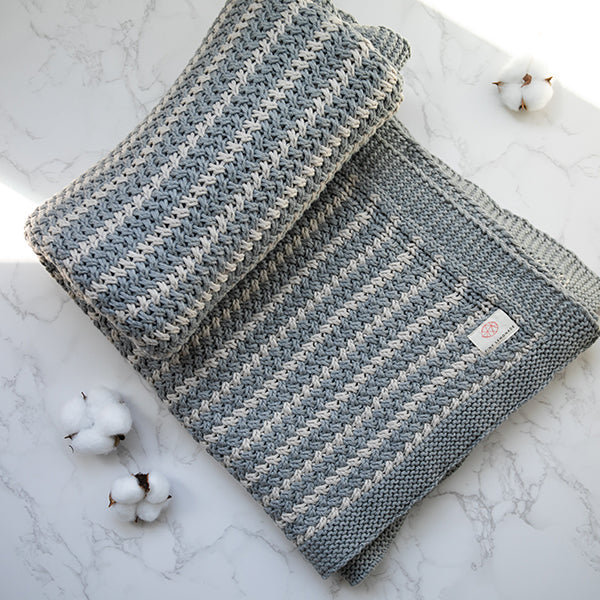 Light gray knit throw blanket with striped pattern and small stitched tag